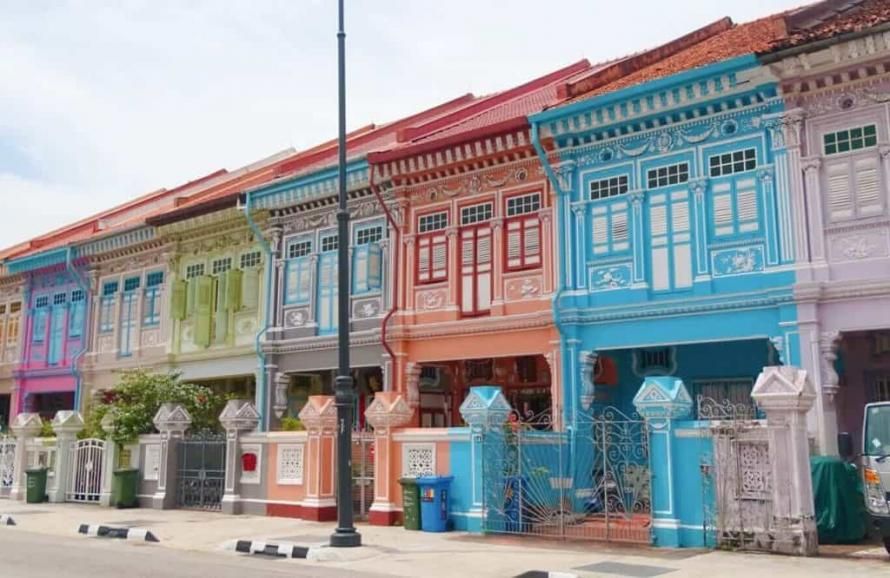 Colorful Peranakan shophouses with ornate facades in pastel pink, green, blue, and orange along a street in Singapore.