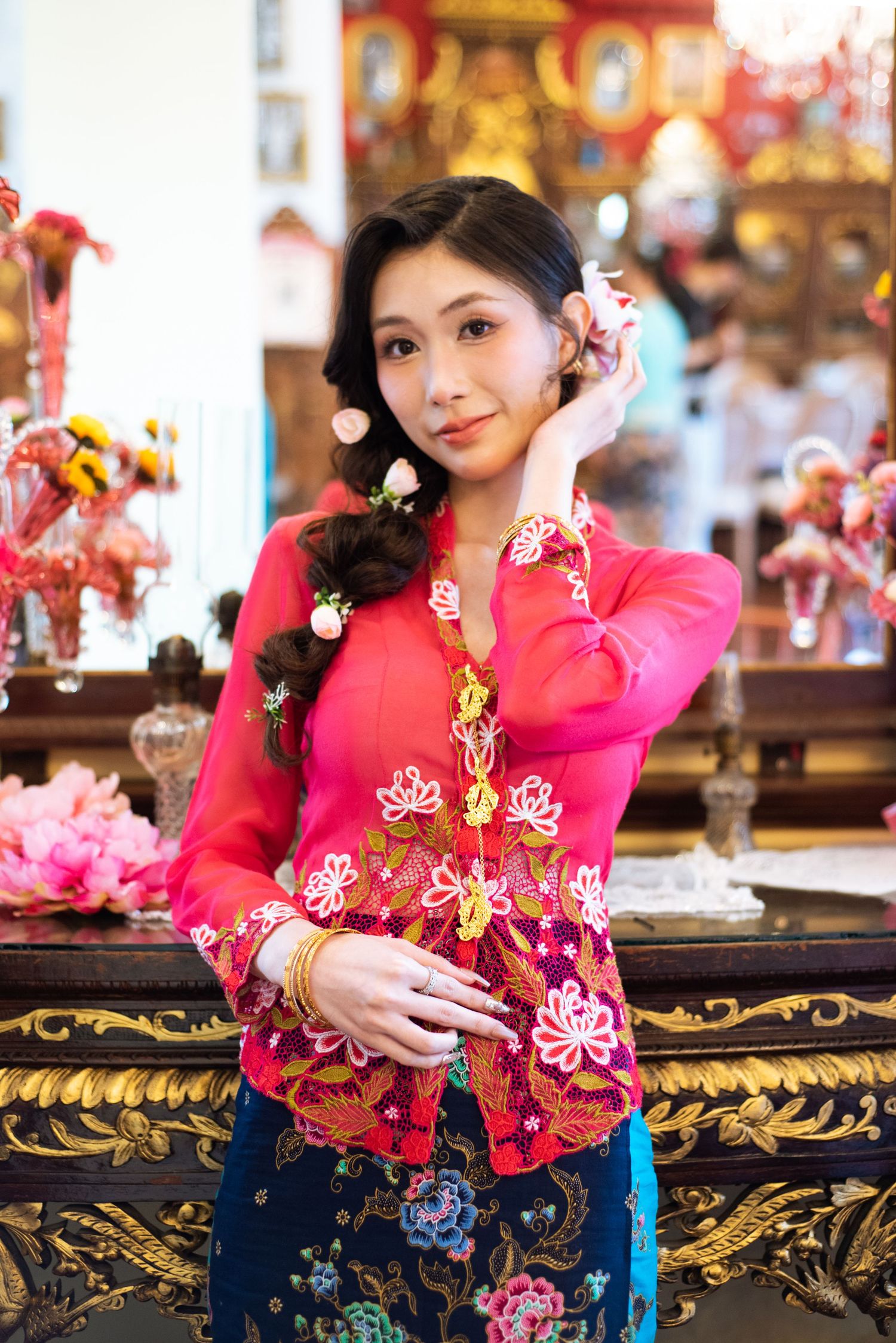 A person wears a vibrant pink traditional Chinese qipao dress with floral embroidery while seated at an ornate table.
