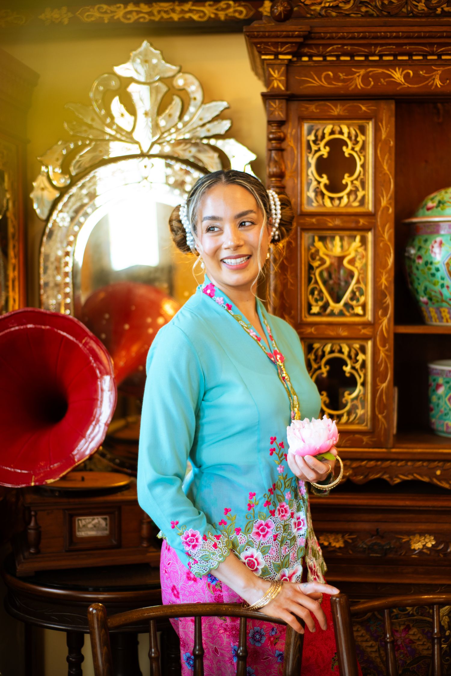 Traditional Balinese dress in turquoise and pink with ornate gold decorations photographed in elegant interior setting.