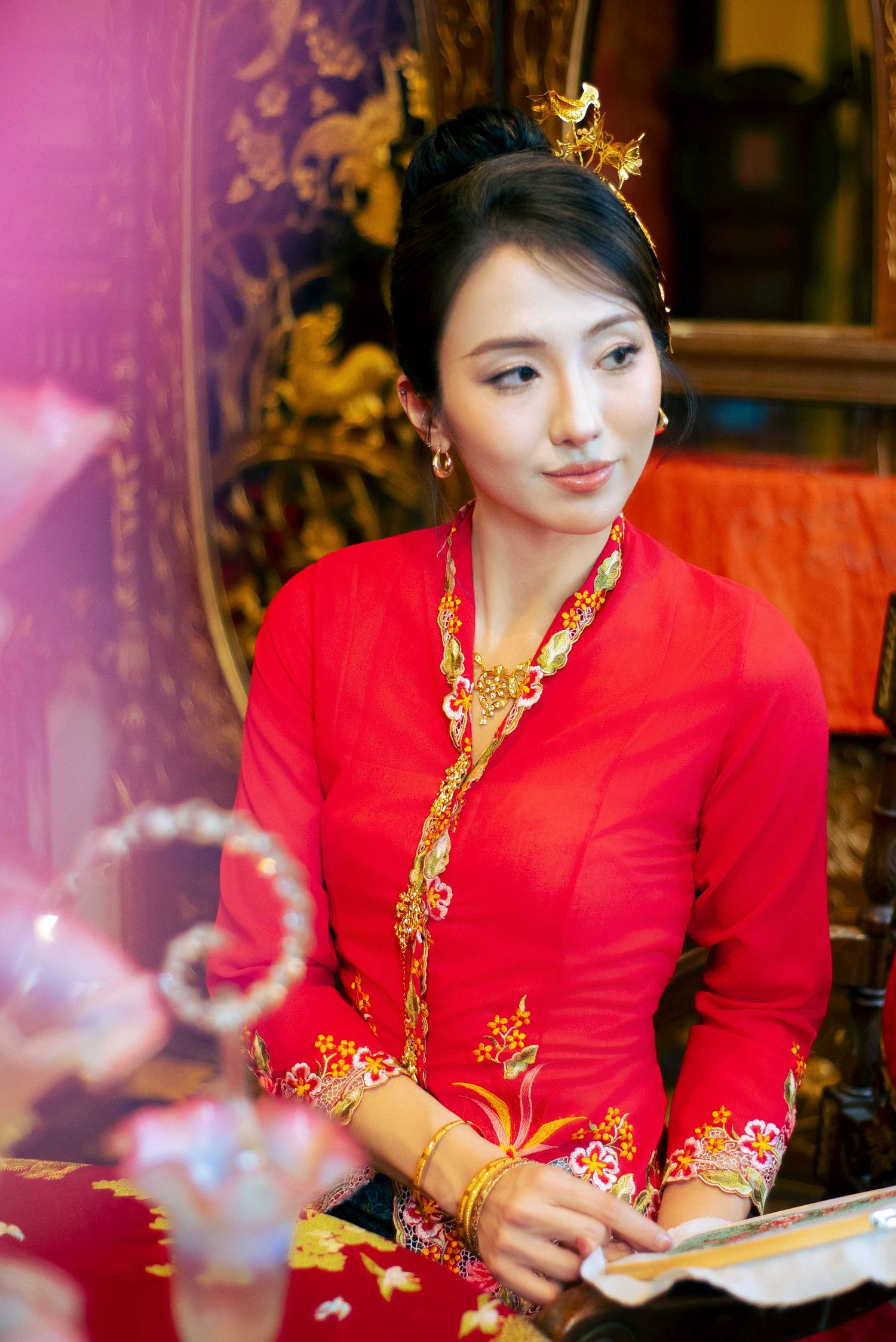 Traditional Chinese wedding attire in bright red with gold embellishments and ornate jewelry in an elegant setting.