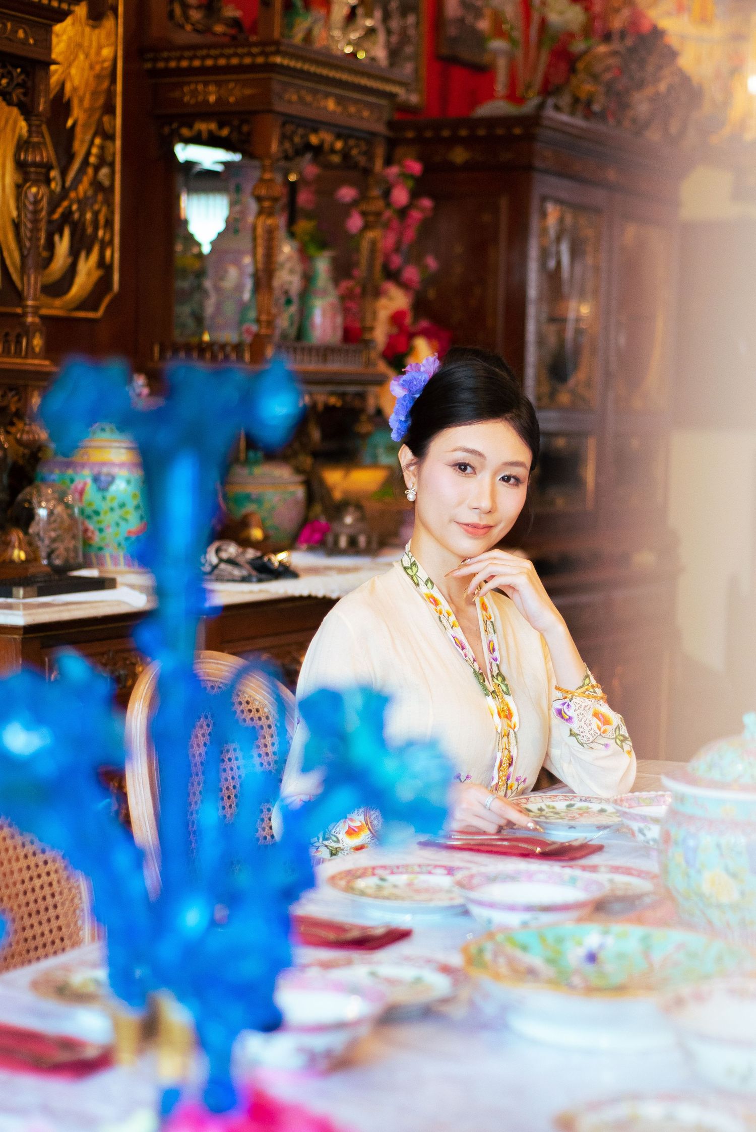 Elegant dining scene with ornate decor, vibrant blue centerpieces, and formal table settings in traditional Asian style.