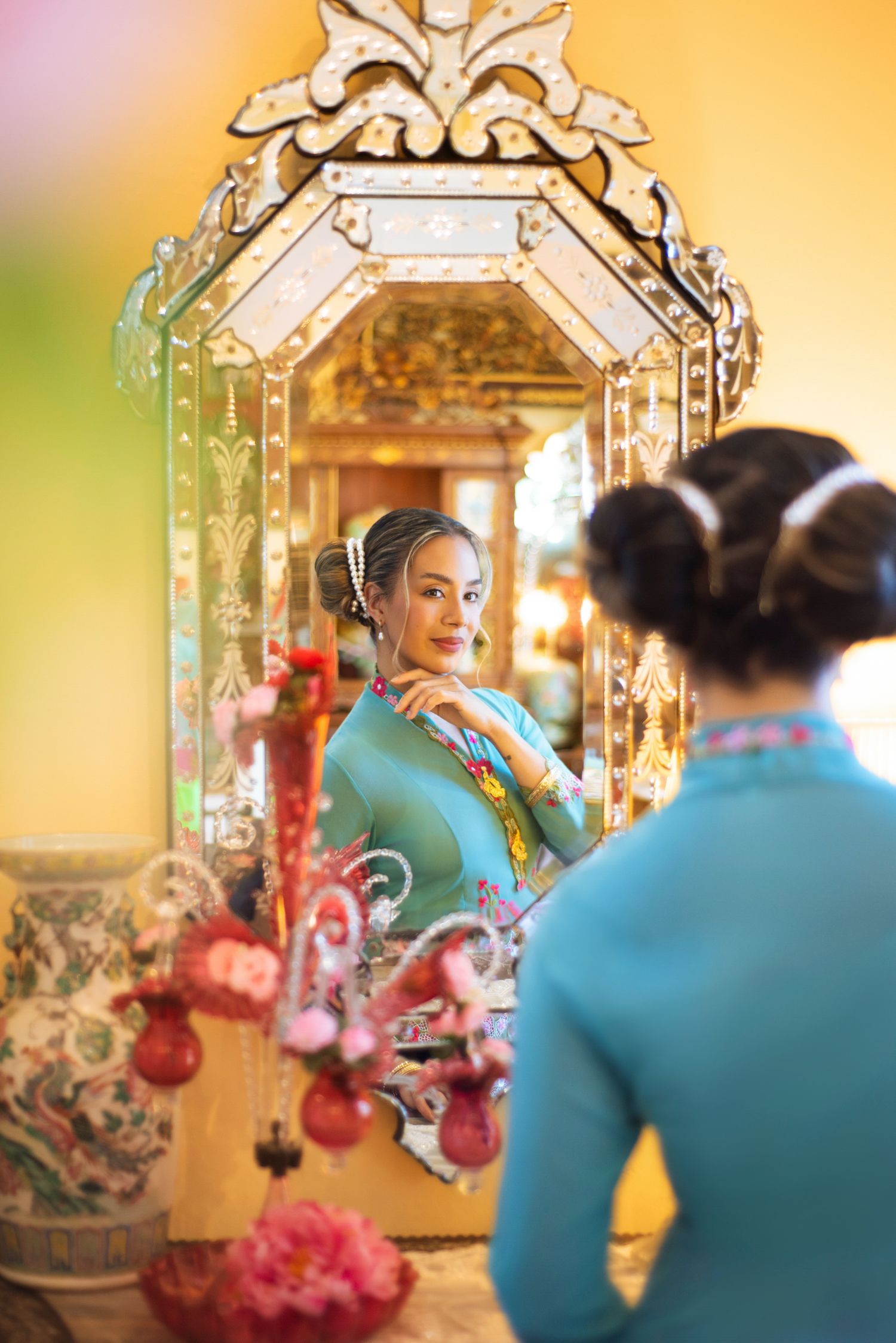 Elegant reflection in an ornate vintage mirror with turquoise clothing and decorative oriental decor in warm lighting.