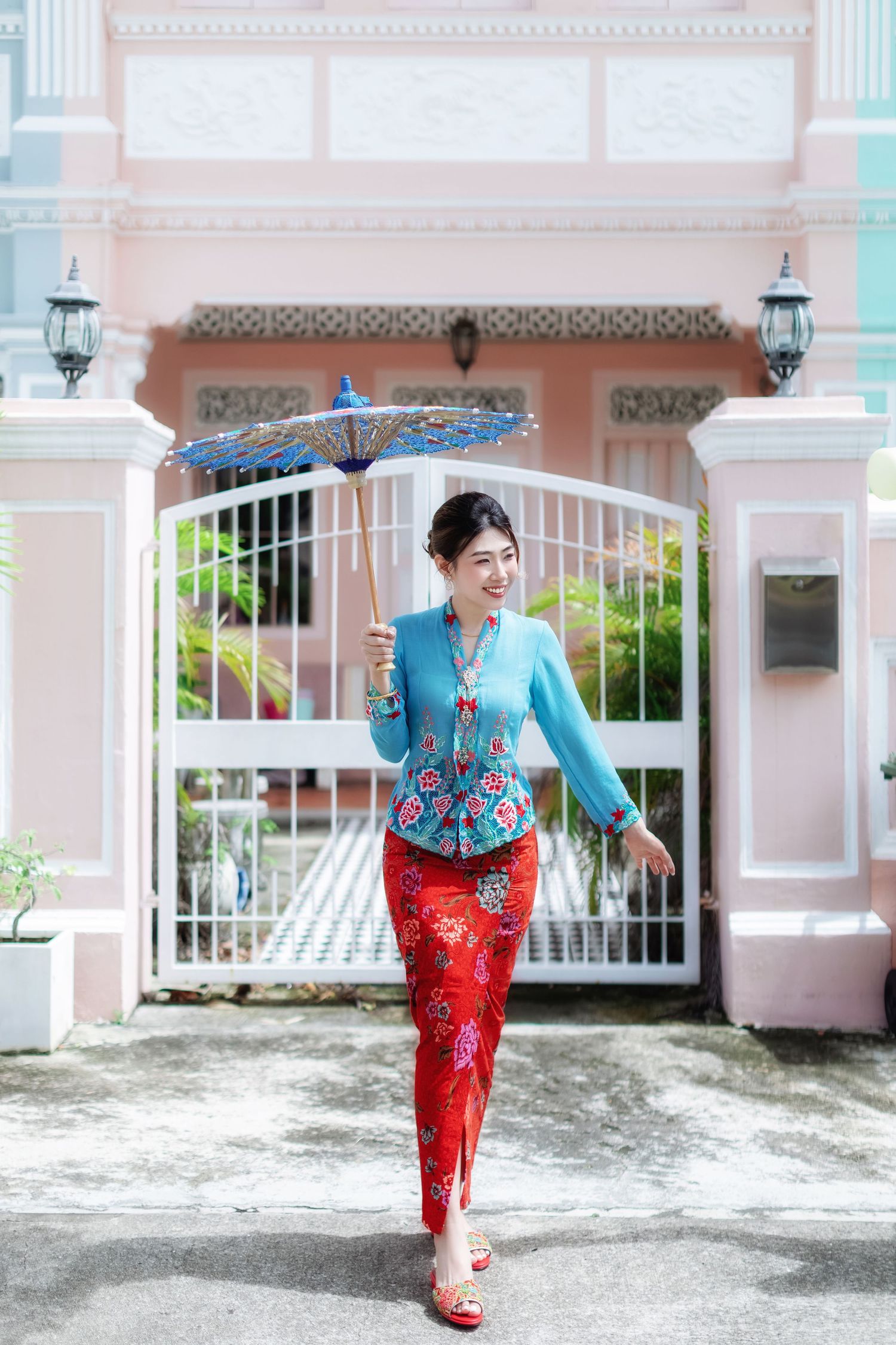 Photo of a Nyonya / Nonya lady in turquoise blue and red traditional Nyonya Kebaya posing in front of a Peranakan house at Joo Chiat
