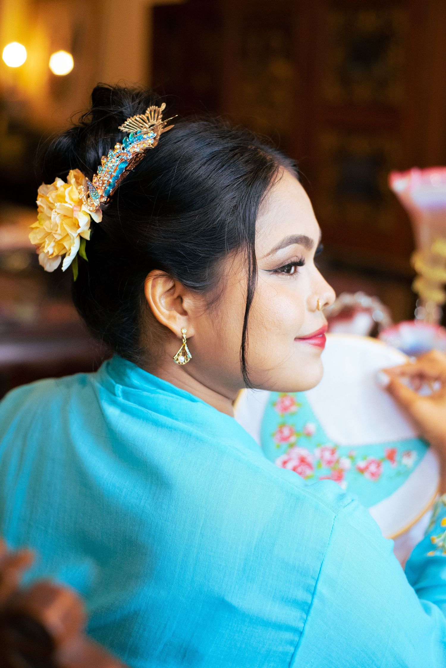 Profile view of someone in a bright turquoise dress wearing an ornate floral hairpiece and delicate earrings.