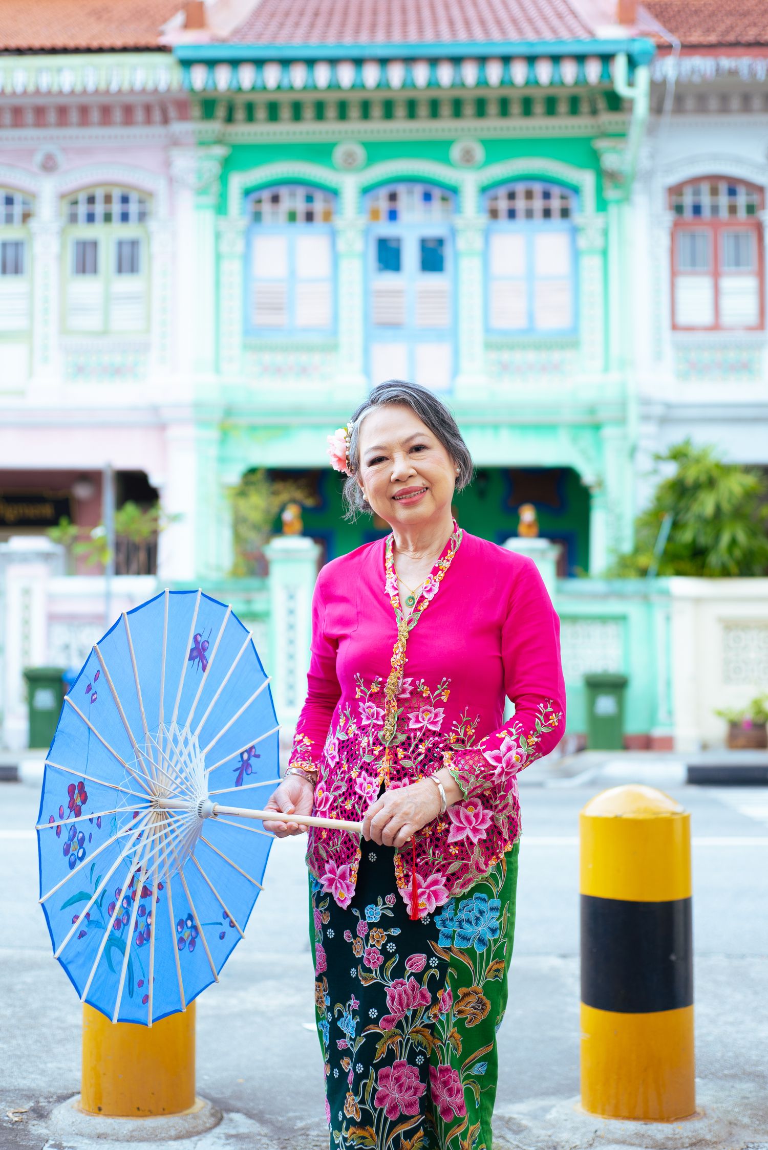 Traditional Peranakan-style photo with bright blue parasol against green heritage shophouse in Singapore's historic district.