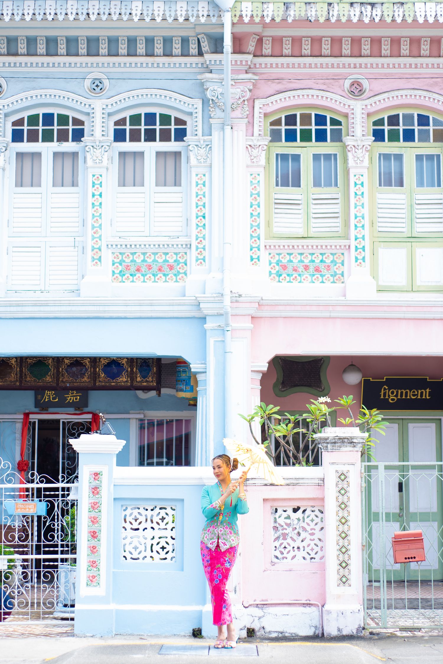 Colorful Peranakan shophouses with ornate architectural details in pastel blue and pink along a Singapore street.