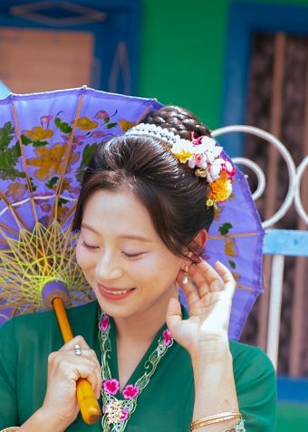 Woman wearing green traditional dress and floral crown enjoying a festive moment in colorful setting.