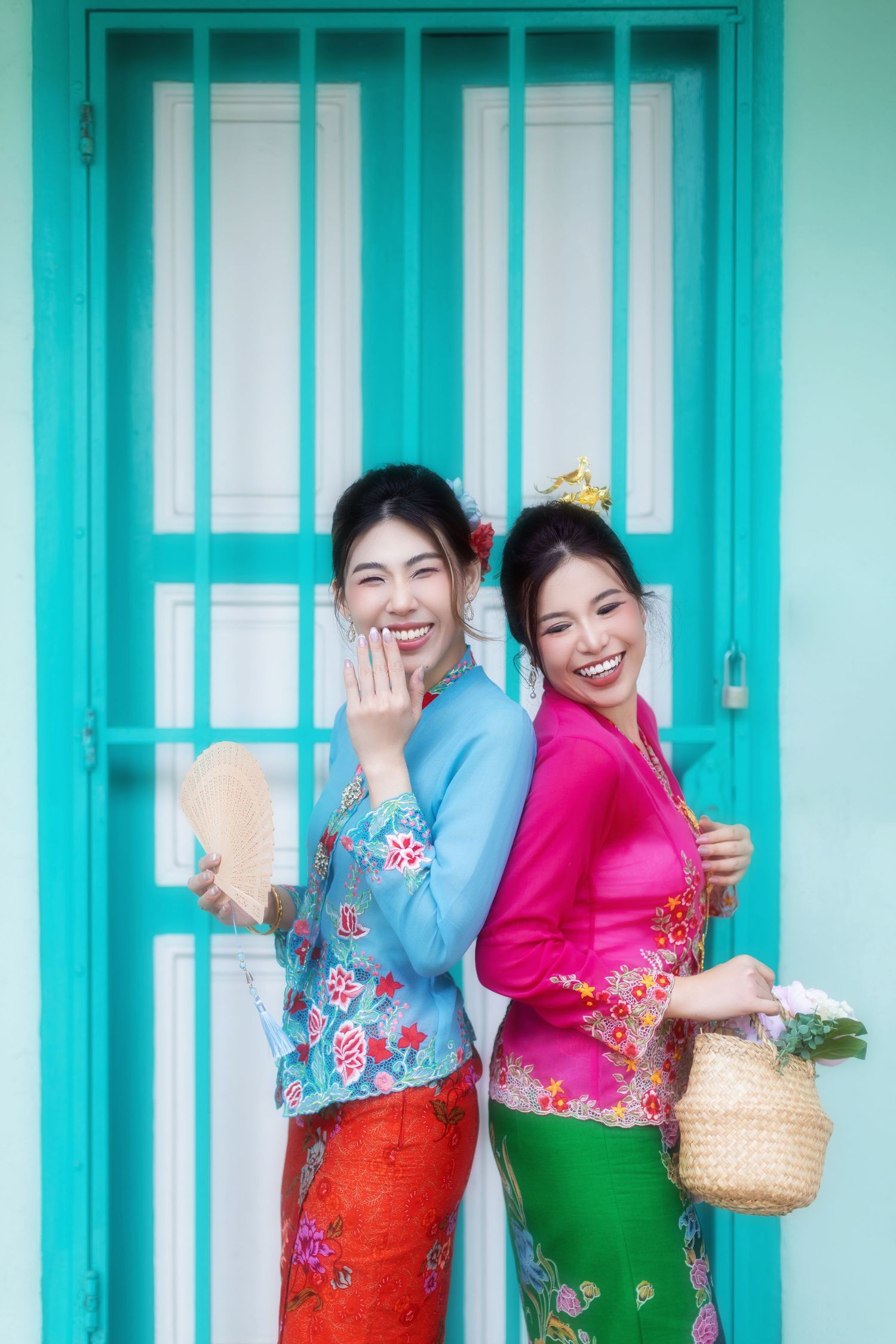 Photoshoot of two friends dressed in traditional Nyonya Kebaya posing against a turquoise Peranakan house at Joo Chiat.