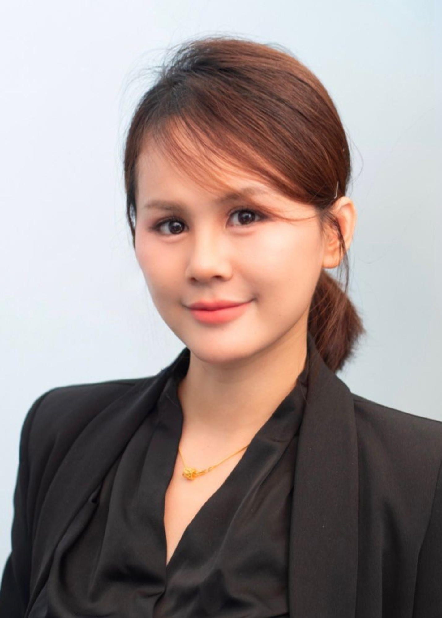 Professional headshot of a person wearing a black business suit and necklace against a light blue background.