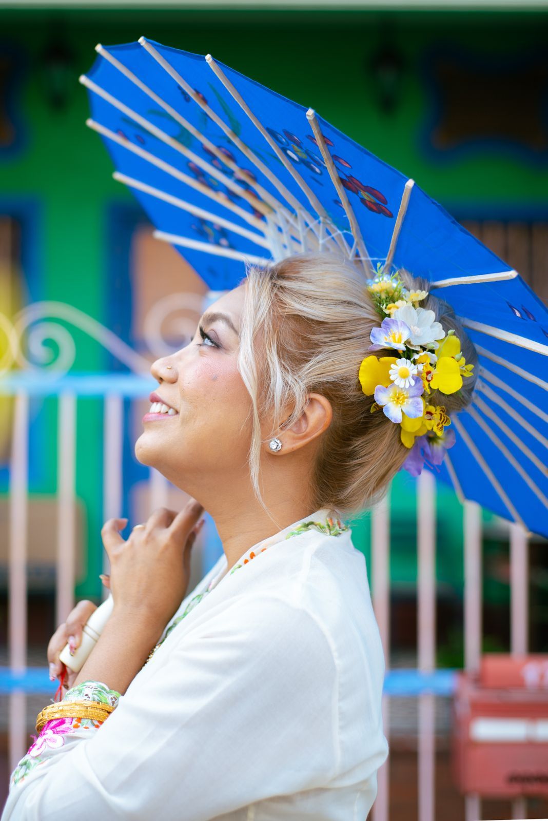 A blue paper parasol frames a joyful moment in traditional Asian attire with yellow and white floral hair ornaments.