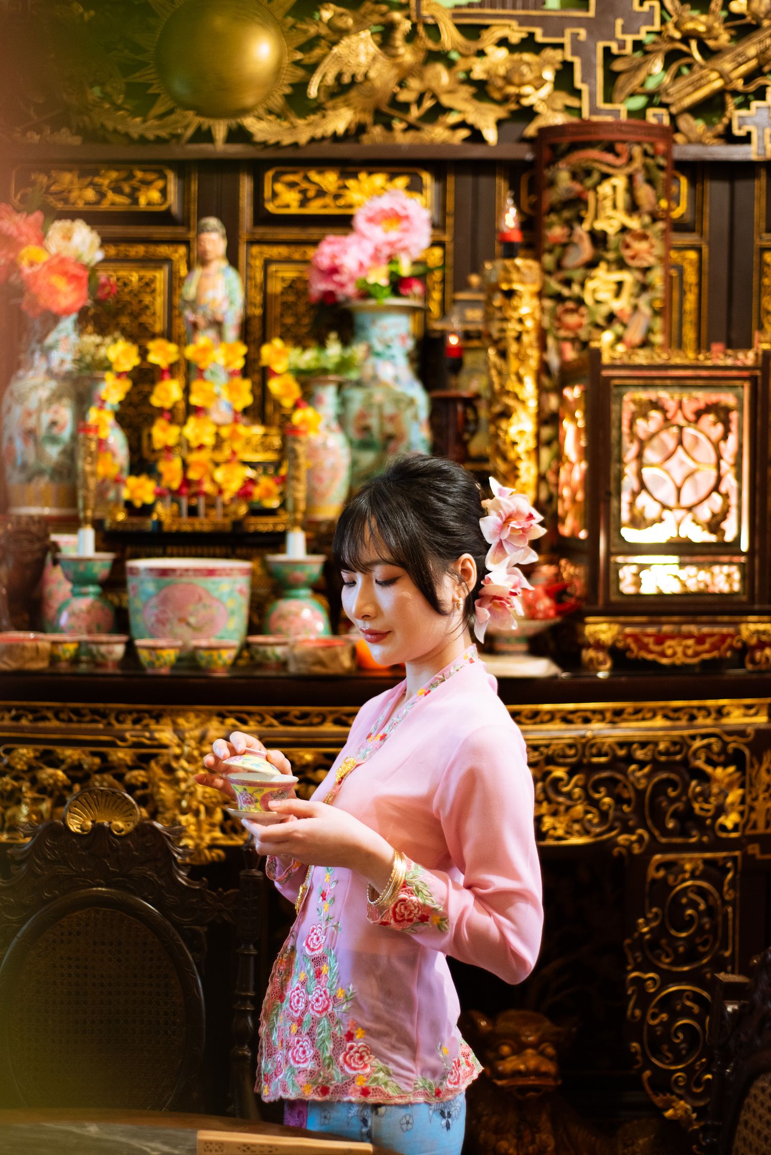 Side view of someone wearing a pink sweater admiring ornate temple decorations in warm golden lighting.