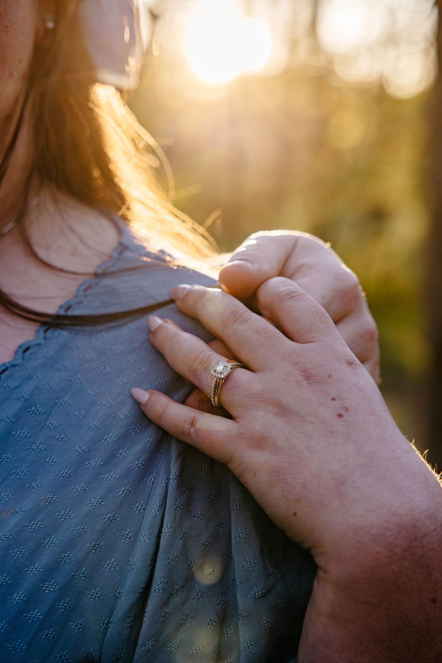 Close-up view of hands engaged in a romantic proposal at sunset with golden light filtering through trees.