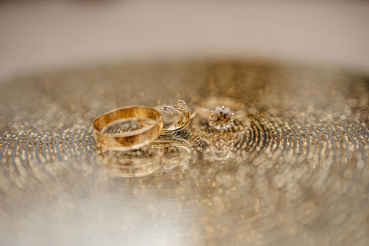 Wedding rings resting on a sparkly glittery surface with soft bokeh lighting effect in macro photography.