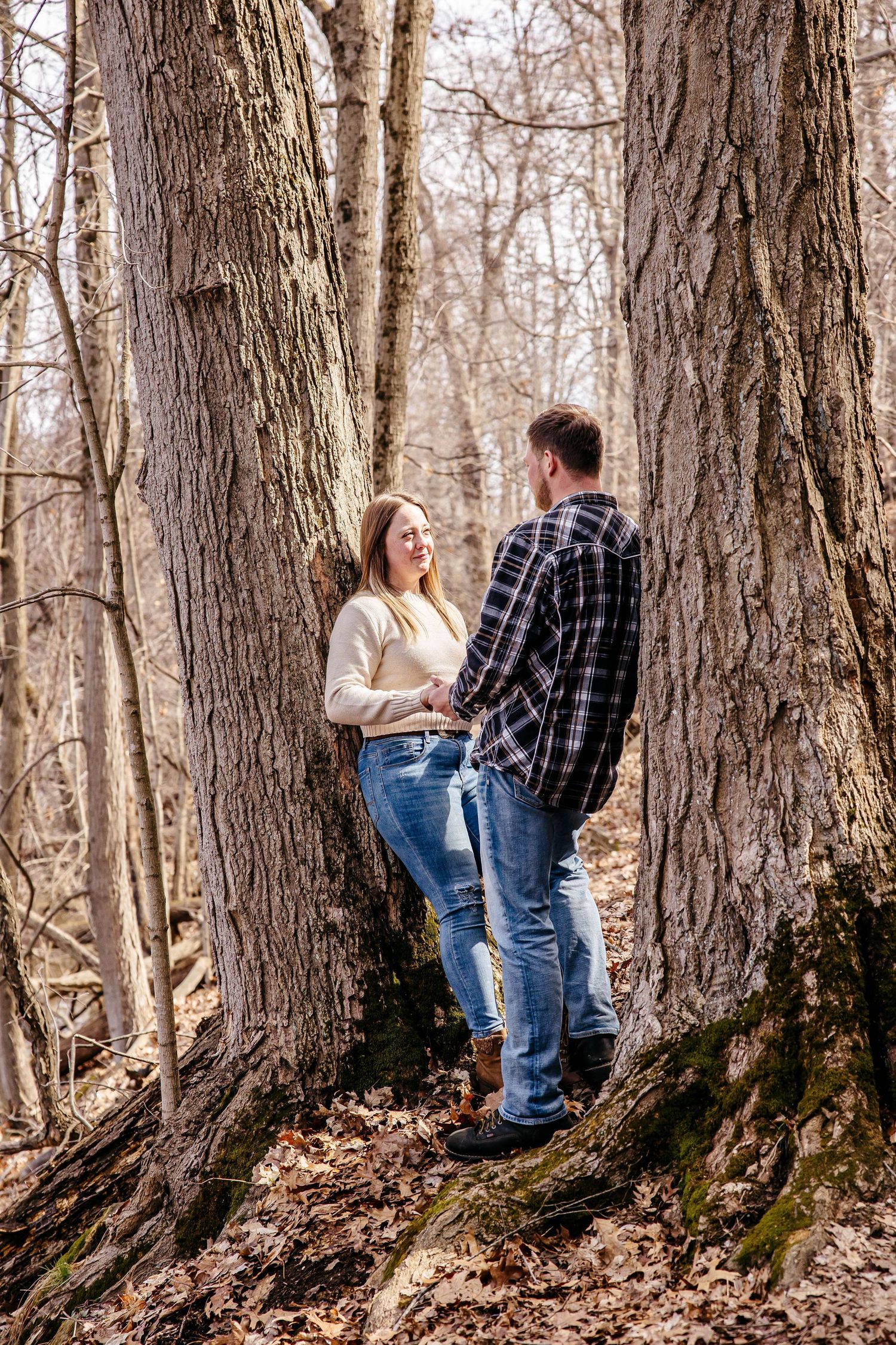 A couple shares romantic moments in a series of photos against large tree trunks in an autumn forest setting.