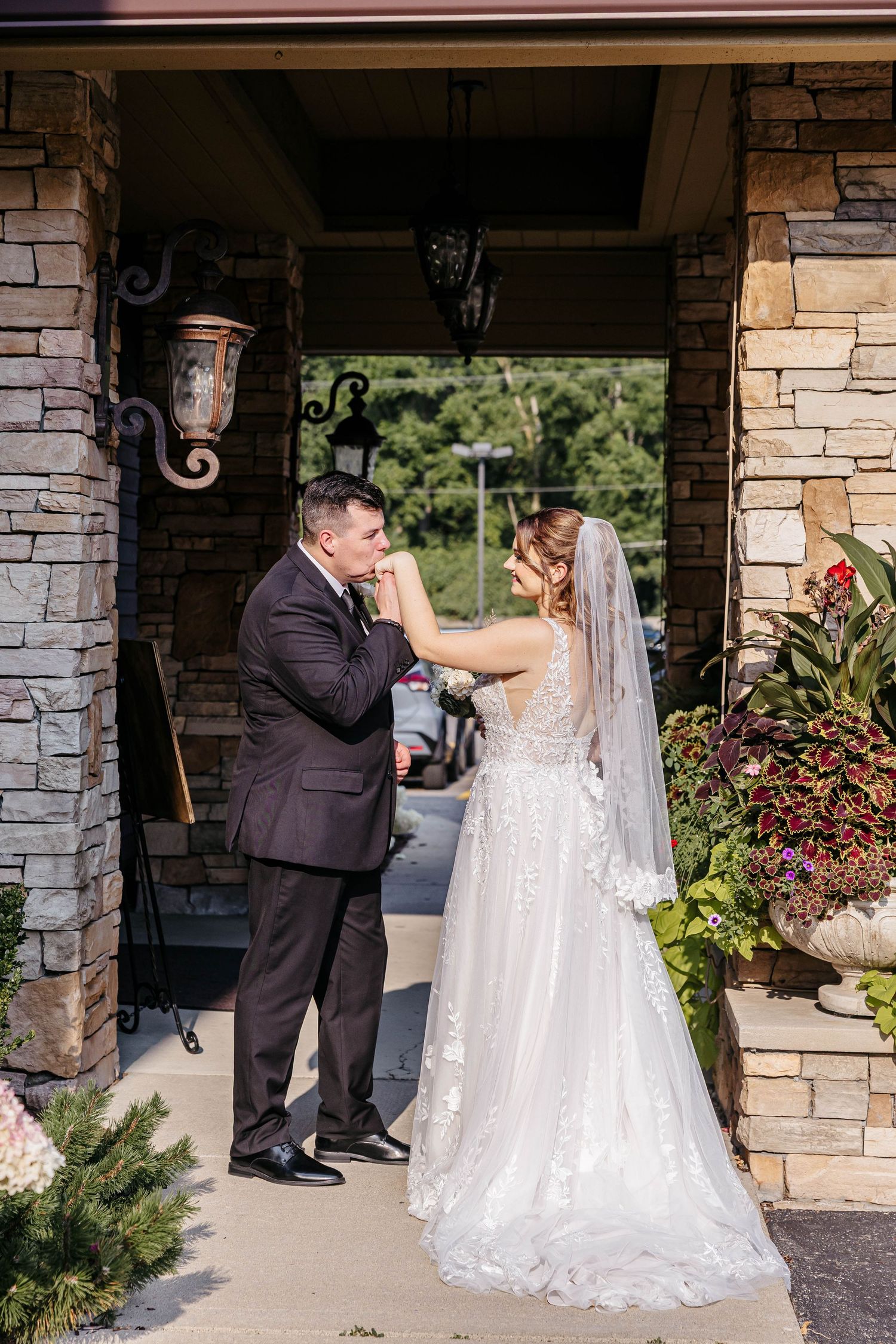 A tender wedding moment captured under a stone archway entrance with decorative sconces and potted plants.