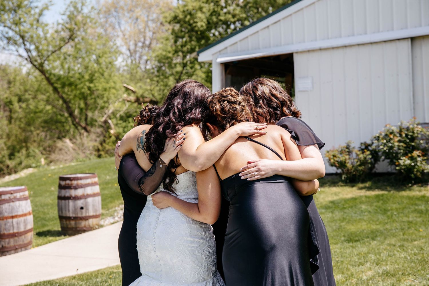 Romantic couples embrace outdoors at rustic venue with wooden barrels and natural scenery in background.