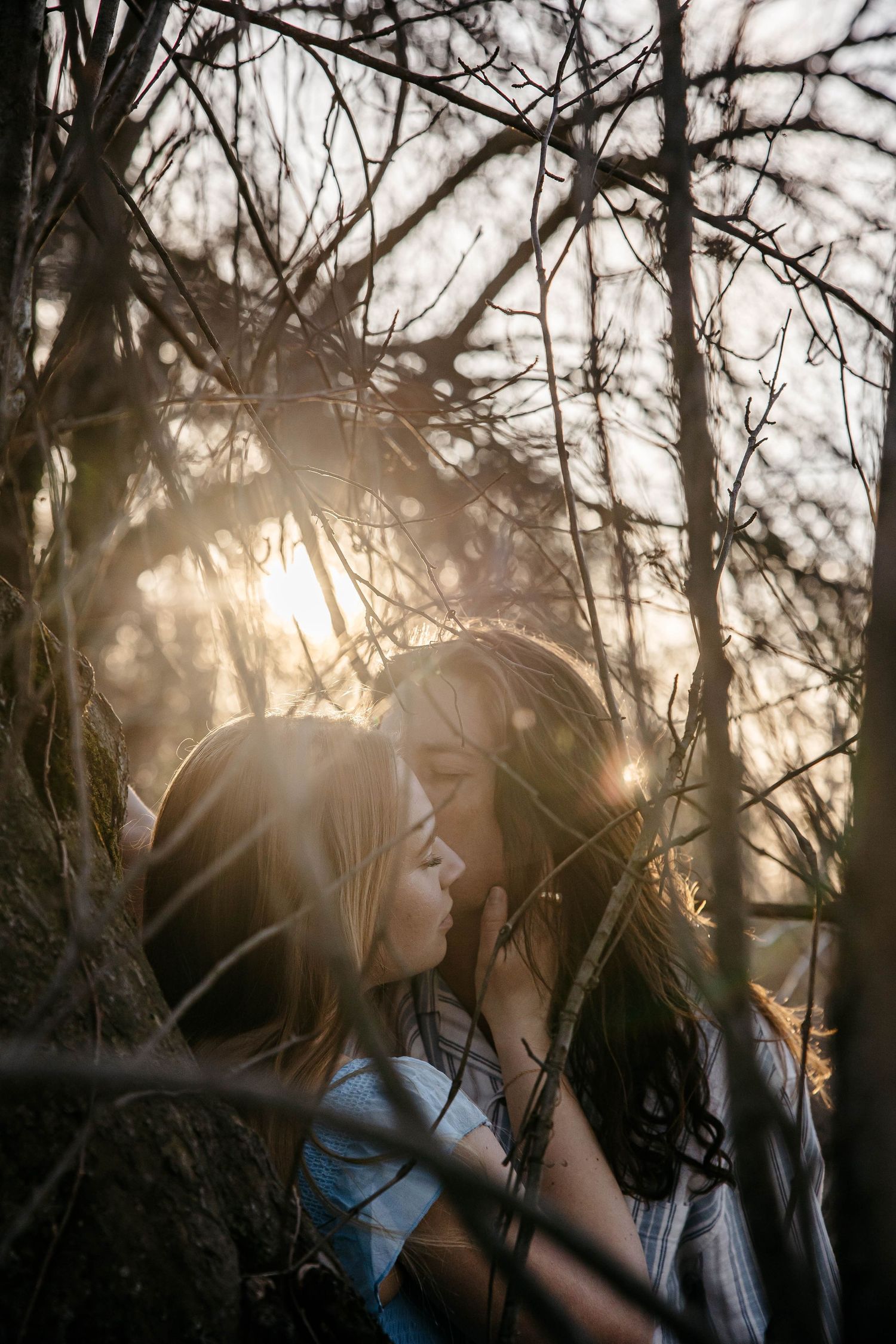 Person photographed from the side against sunlight filtering through bare tree branches in a moody winter scene.