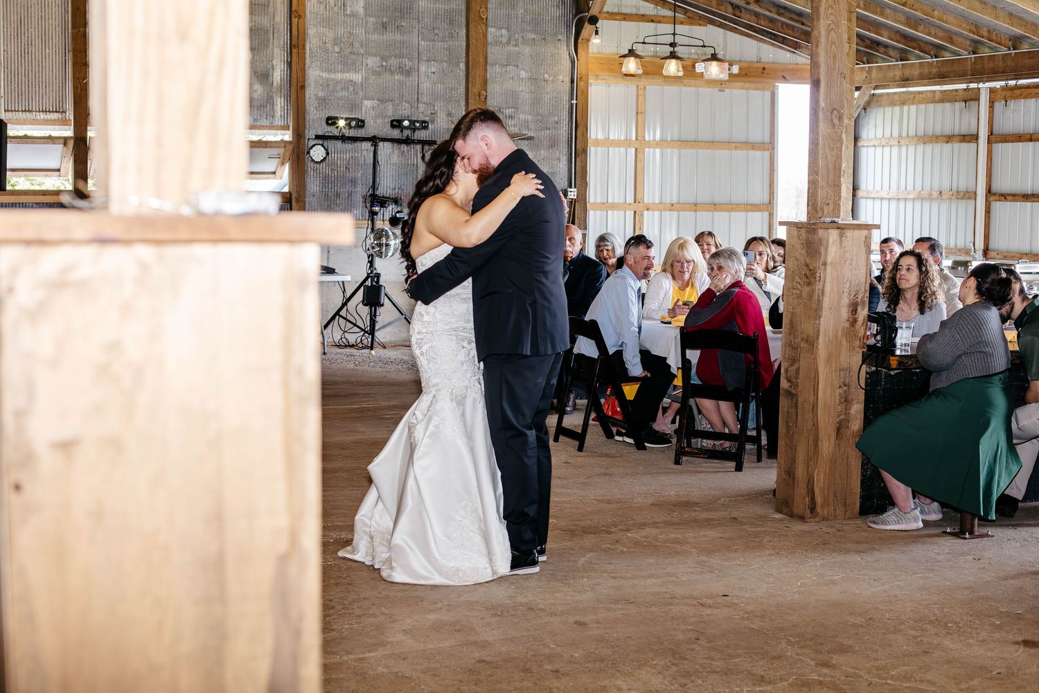 Couples dance together at a rustic barn wedding reception under wooden beams and string lights.