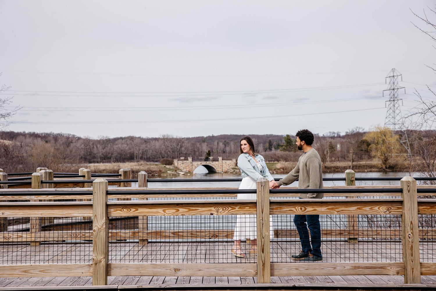 Two people interact on a wooden observation deck overlooking a scenic winter landscape with power lines in the distance.