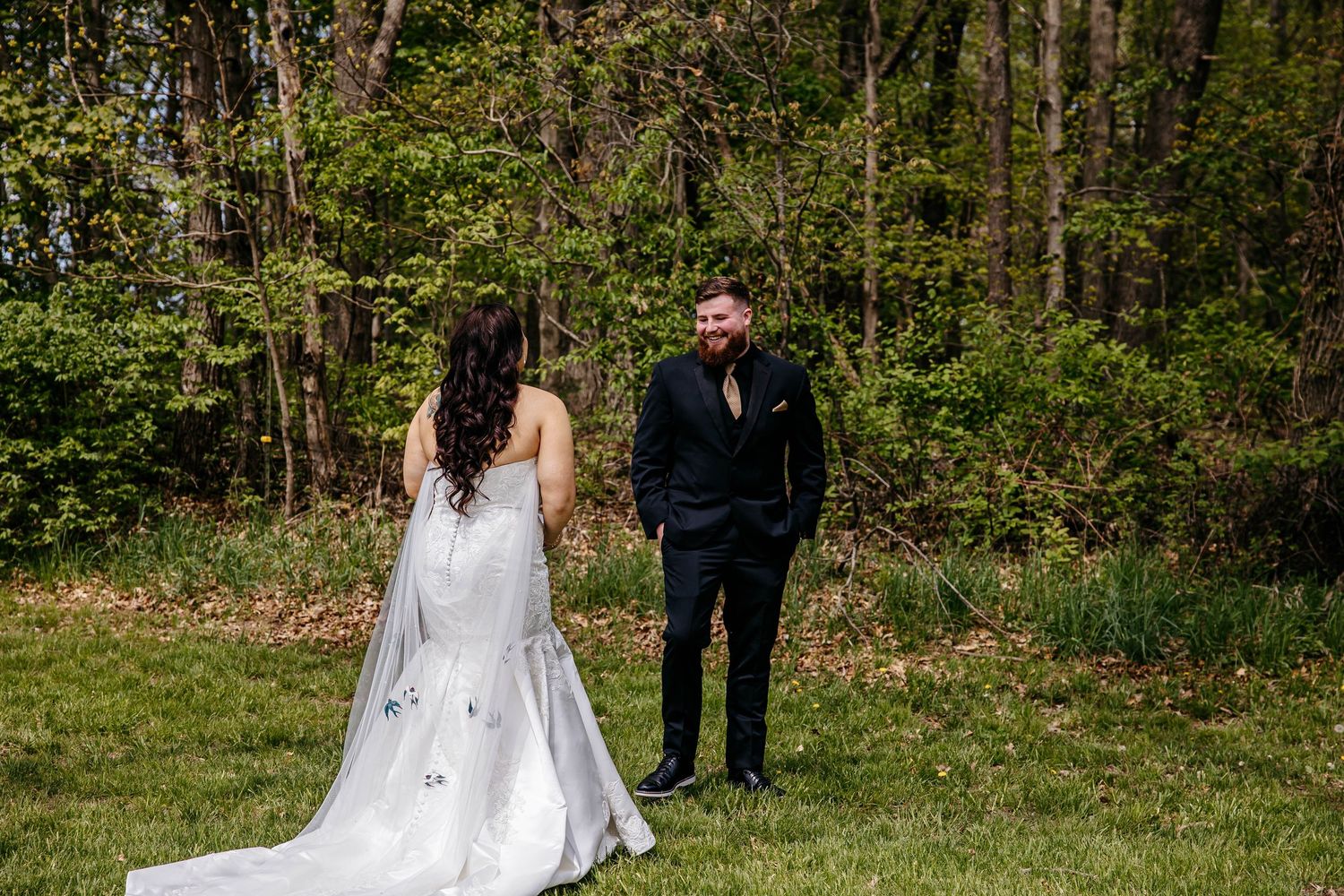 A couple shares their first look moment in a sunlit forest clearing during an outdoor wedding ceremony.