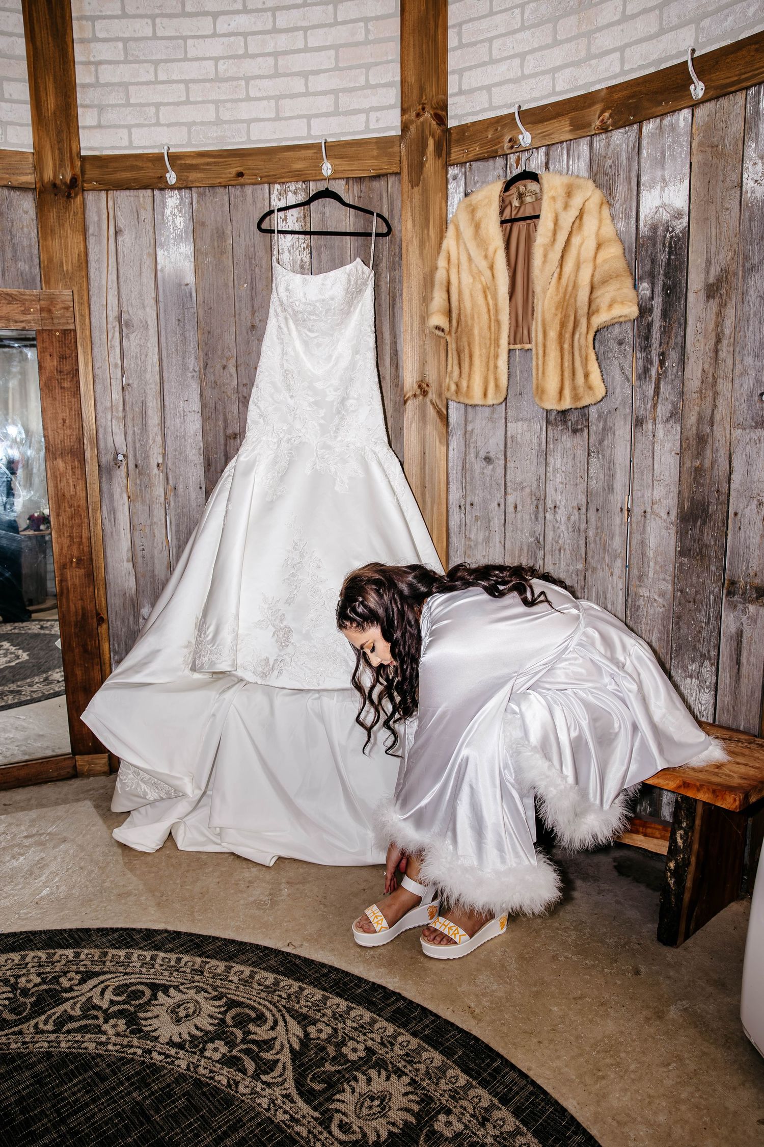 White wedding gowns and beige bridesmaid dresses hang on hangers against a rustic brick and wood wall interior.