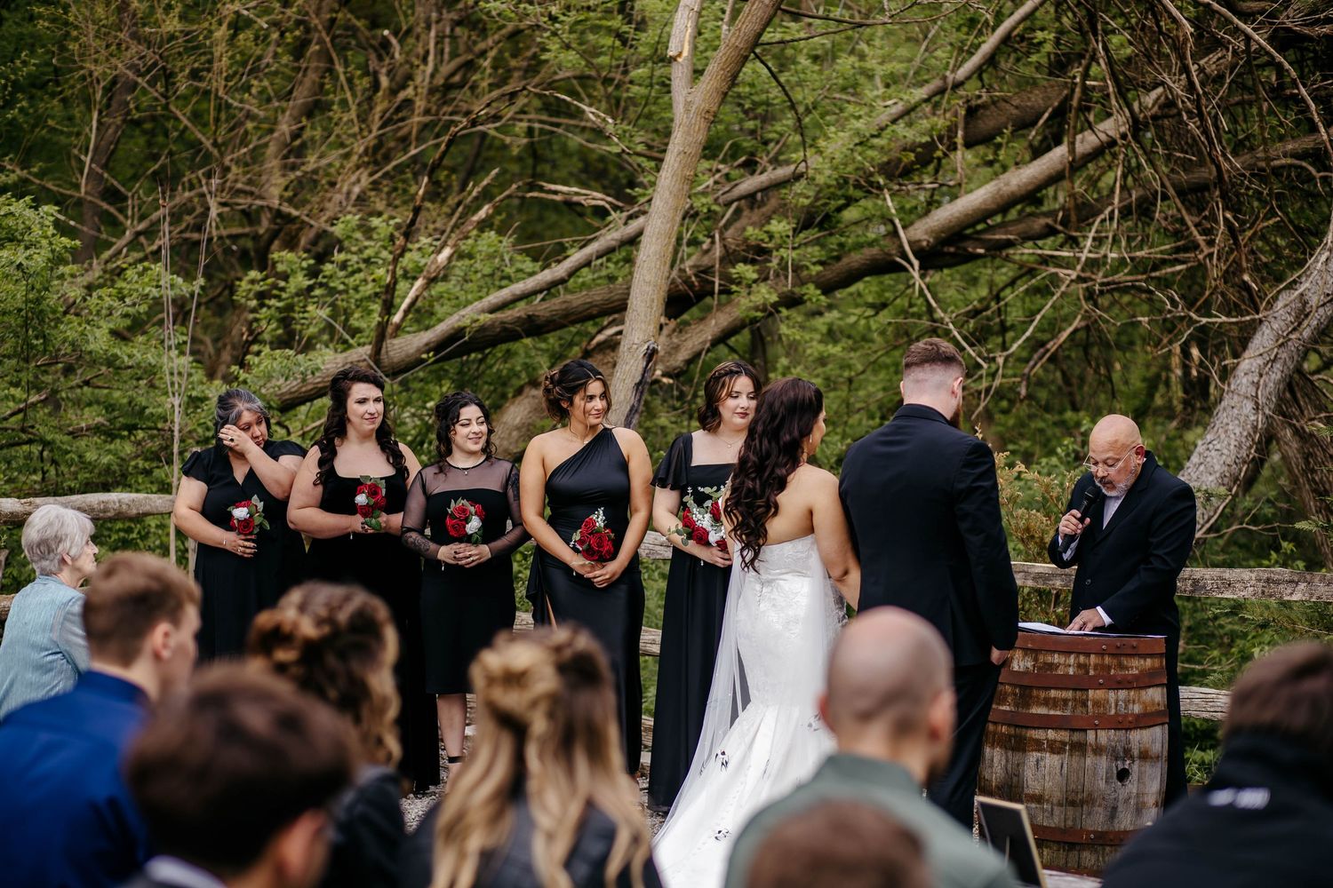 Outdoor wedding ceremony in a wooded setting with guests seated in rows watching the couple exchange vows.
