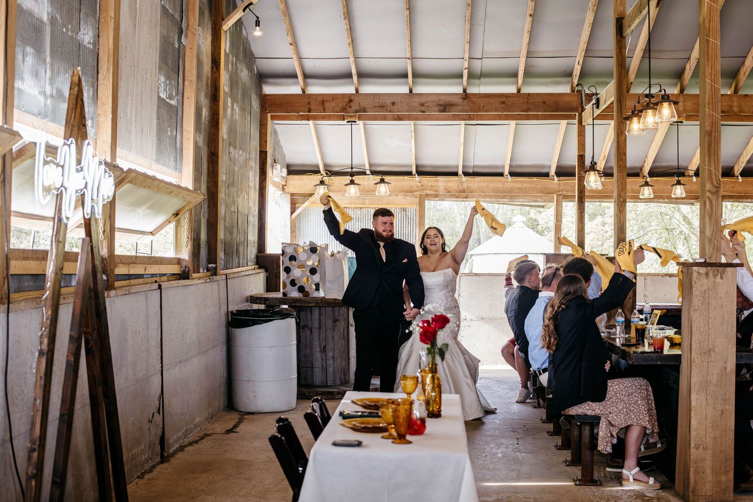 Newlywed couple celebrates with guests inside a rustic barn reception venue filled with natural light.