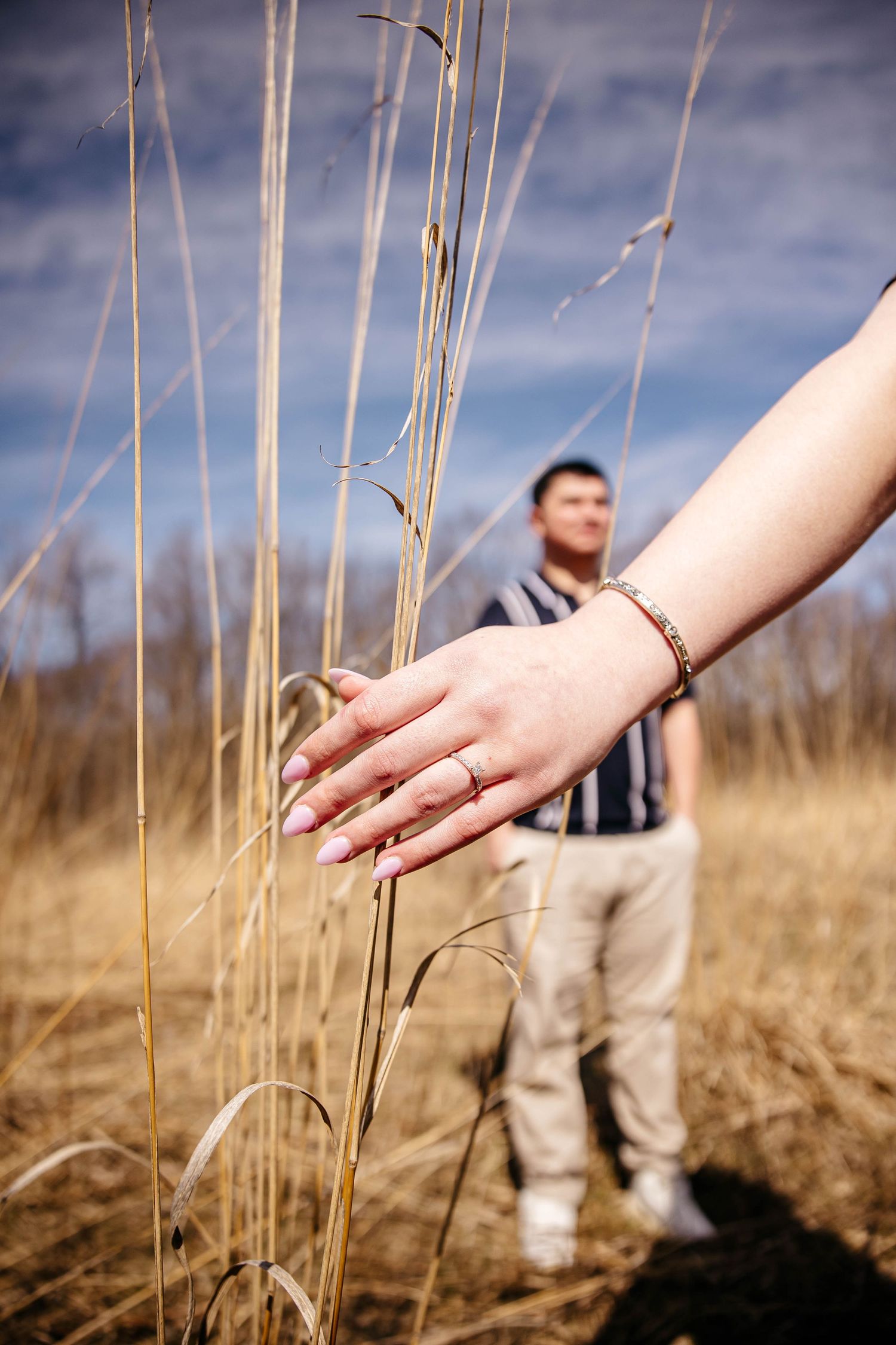 Hand gently brushing against tall dried grass stalks in a golden autumn field with blurred background.