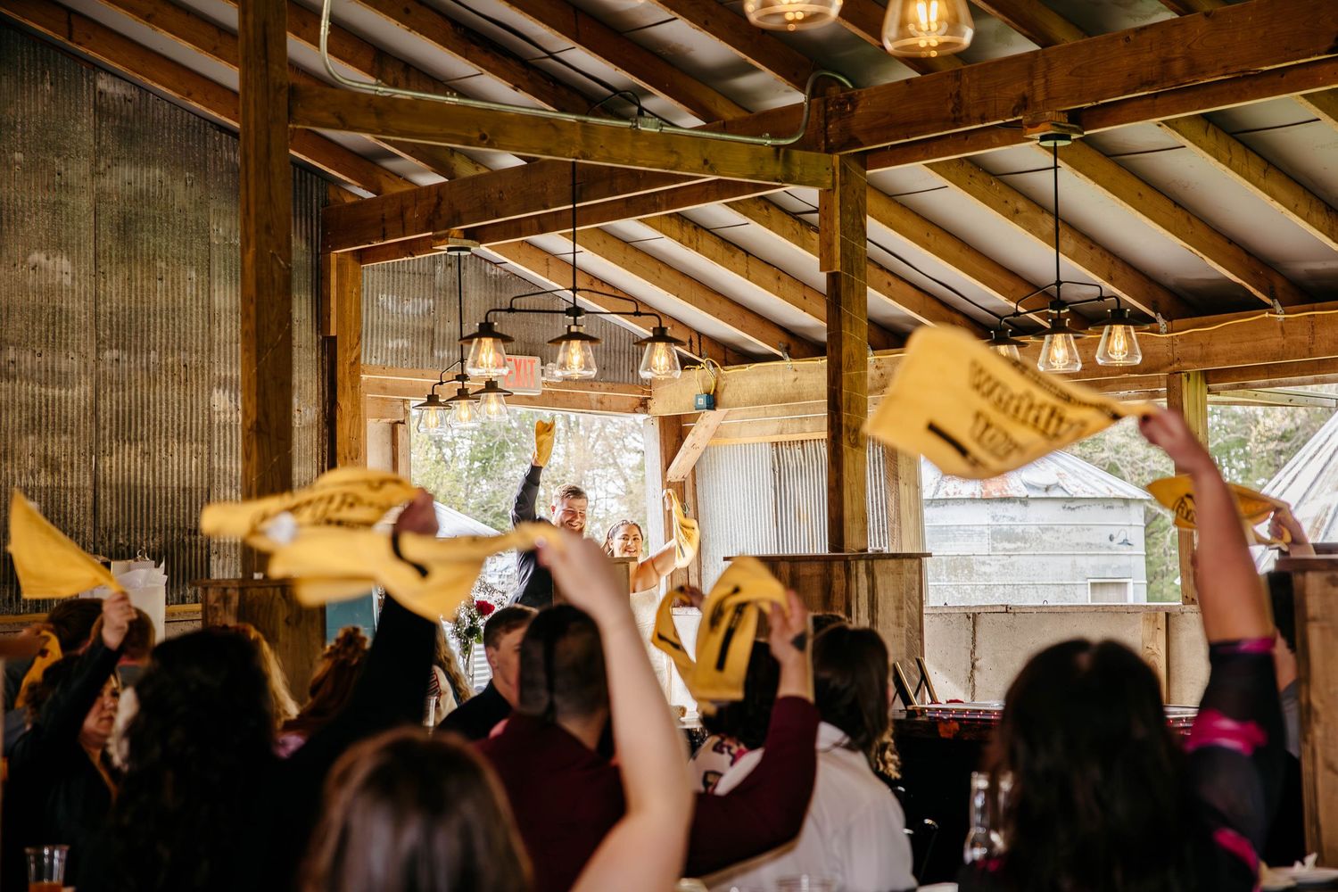 Crowd celebrating at a rustic venue with vaulted wooden beams and raised phones during an indoor event.