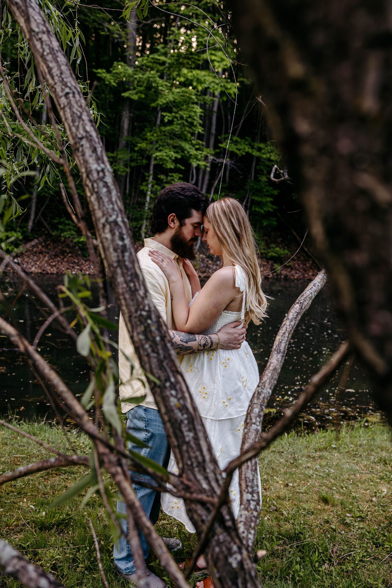 Romantic couple embraces in a wooded forest setting with sunlight filtering through the trees on a summer day.