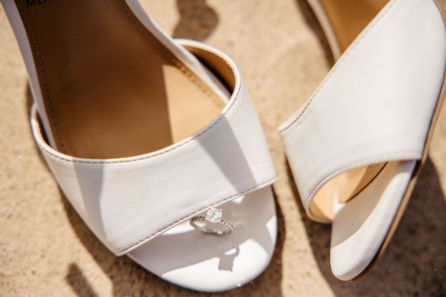 Elegant white patent leather bridal shoes with peep-toe design sitting in natural sunlight.