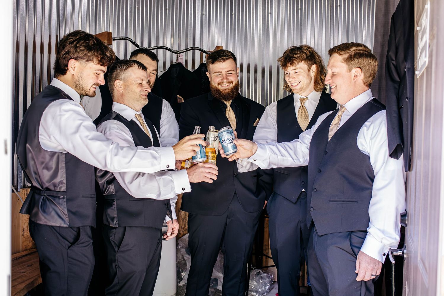Groomsmen in dark suits and vests laughing and celebrating together at a formal event.