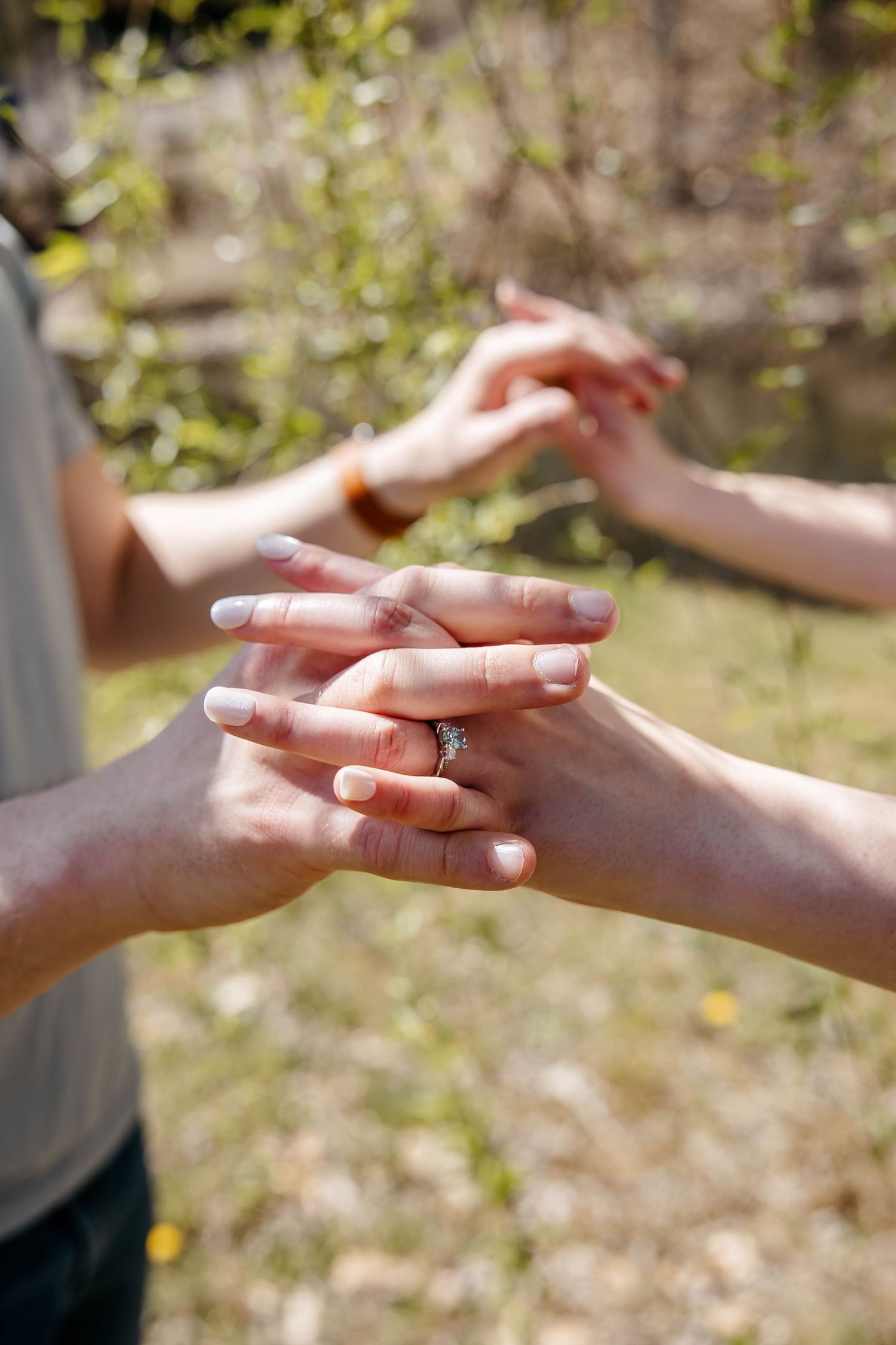 Two hands gently intertwined with a wedding ring visible in natural outdoor lighting.