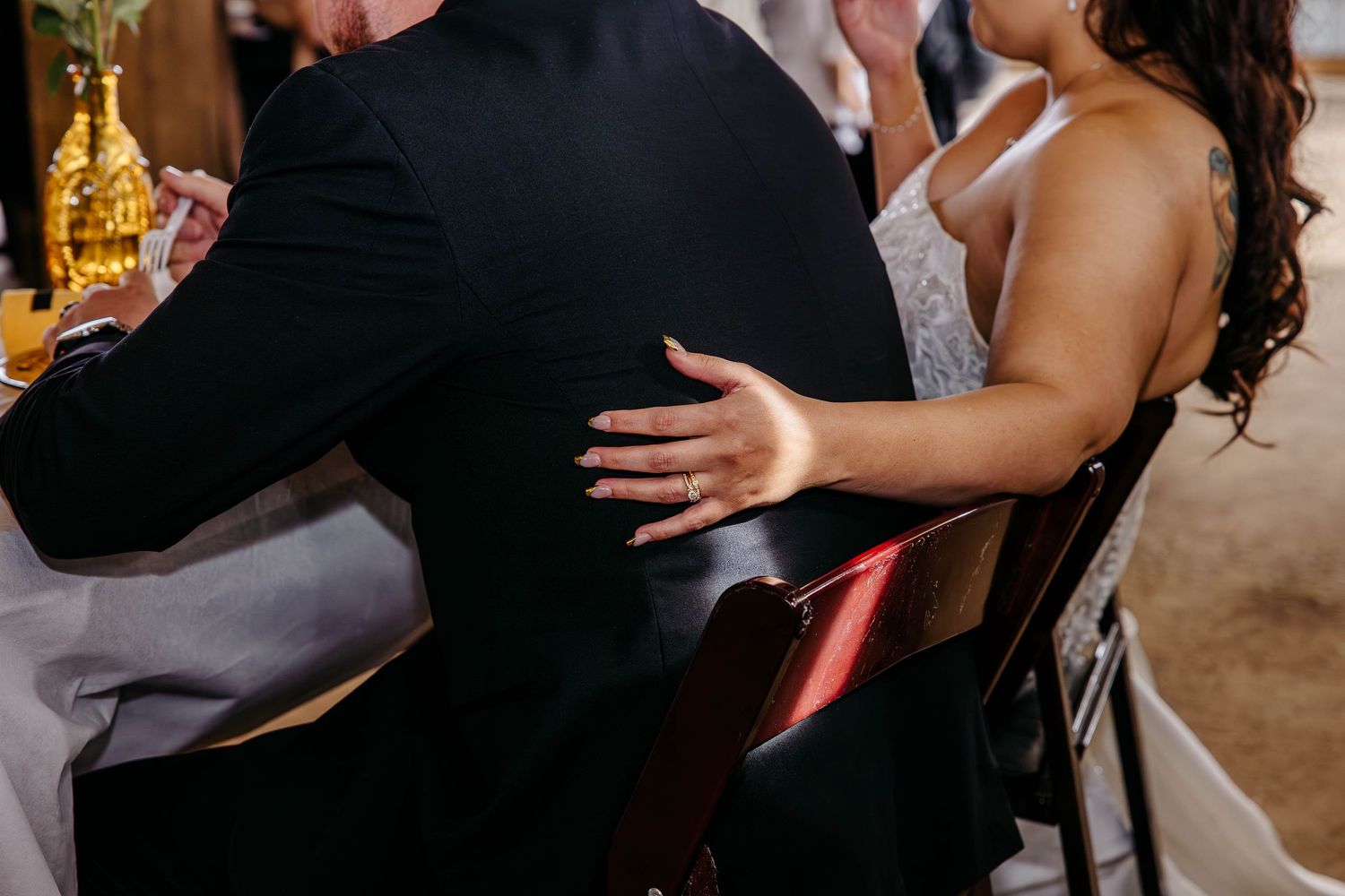Cropped view of couple embracing at wedding reception with guest in black suit and sparkly white dress.
