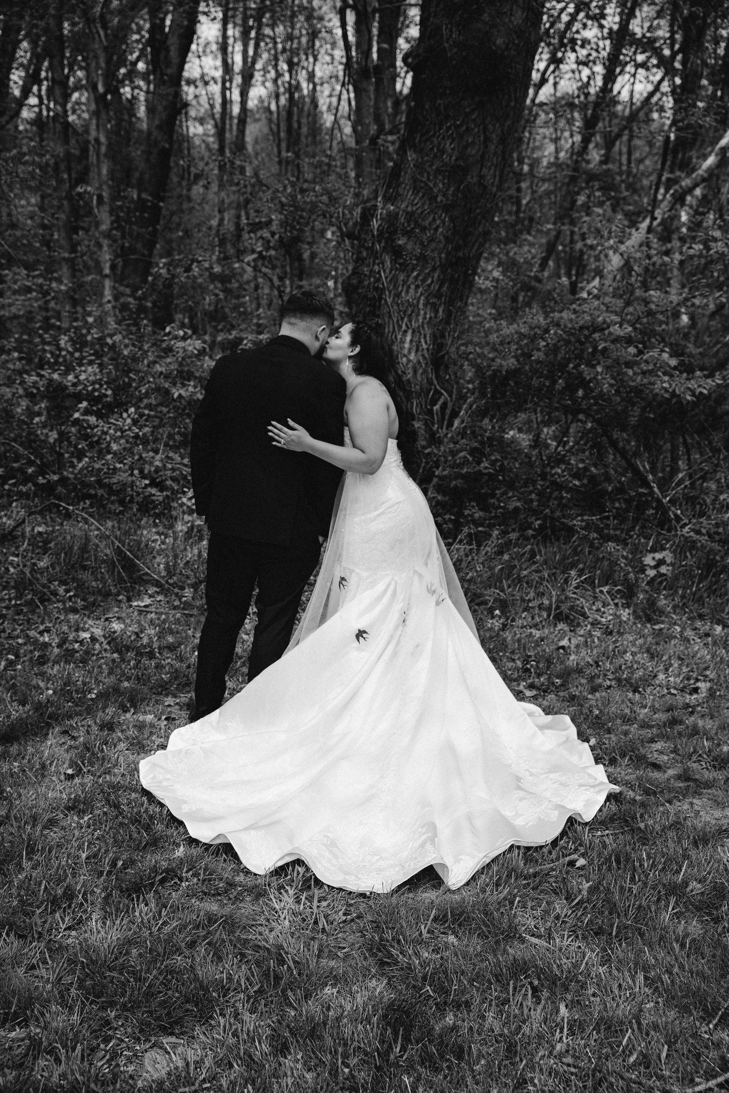 A romantic black and white photograph series showing a couple in wedding attire dancing and embracing in a forest setting.