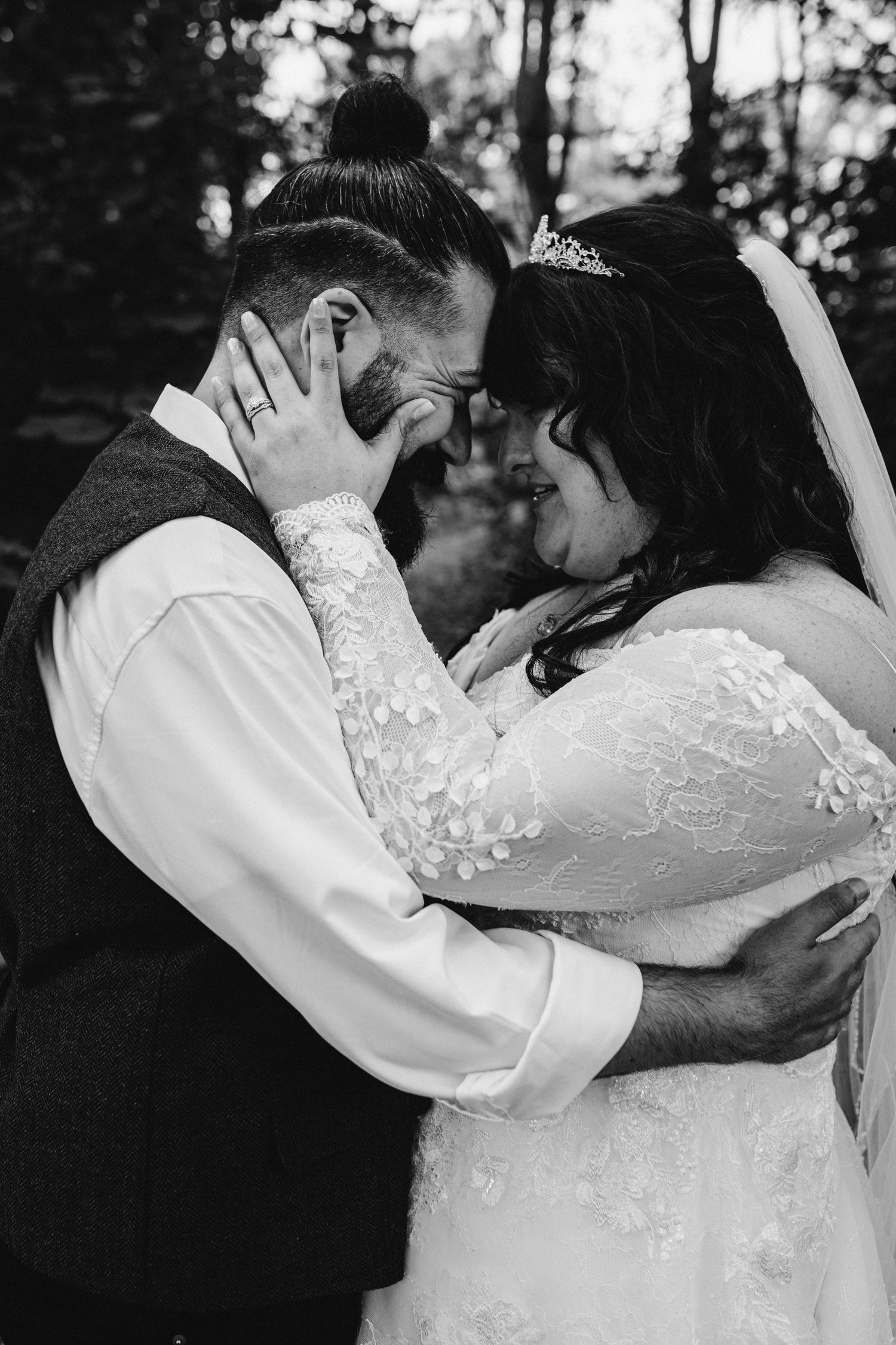 A tender black and white wedding moment captured between newlyweds sharing an intimate embrace outdoors.