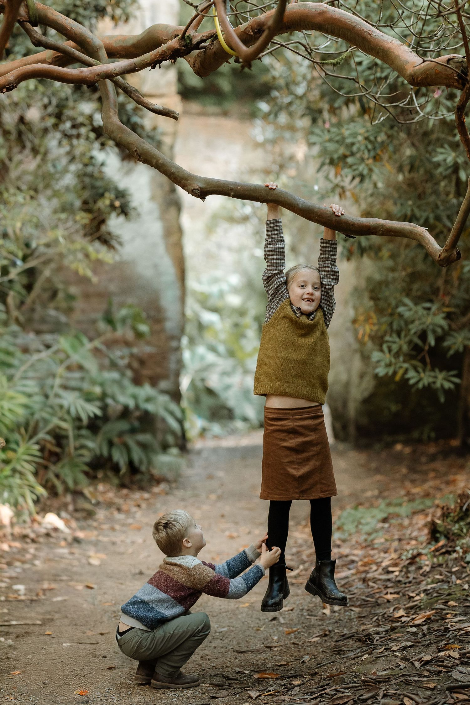 Two people interact playfully beneath a curved tree branch in a misty forest setting.
