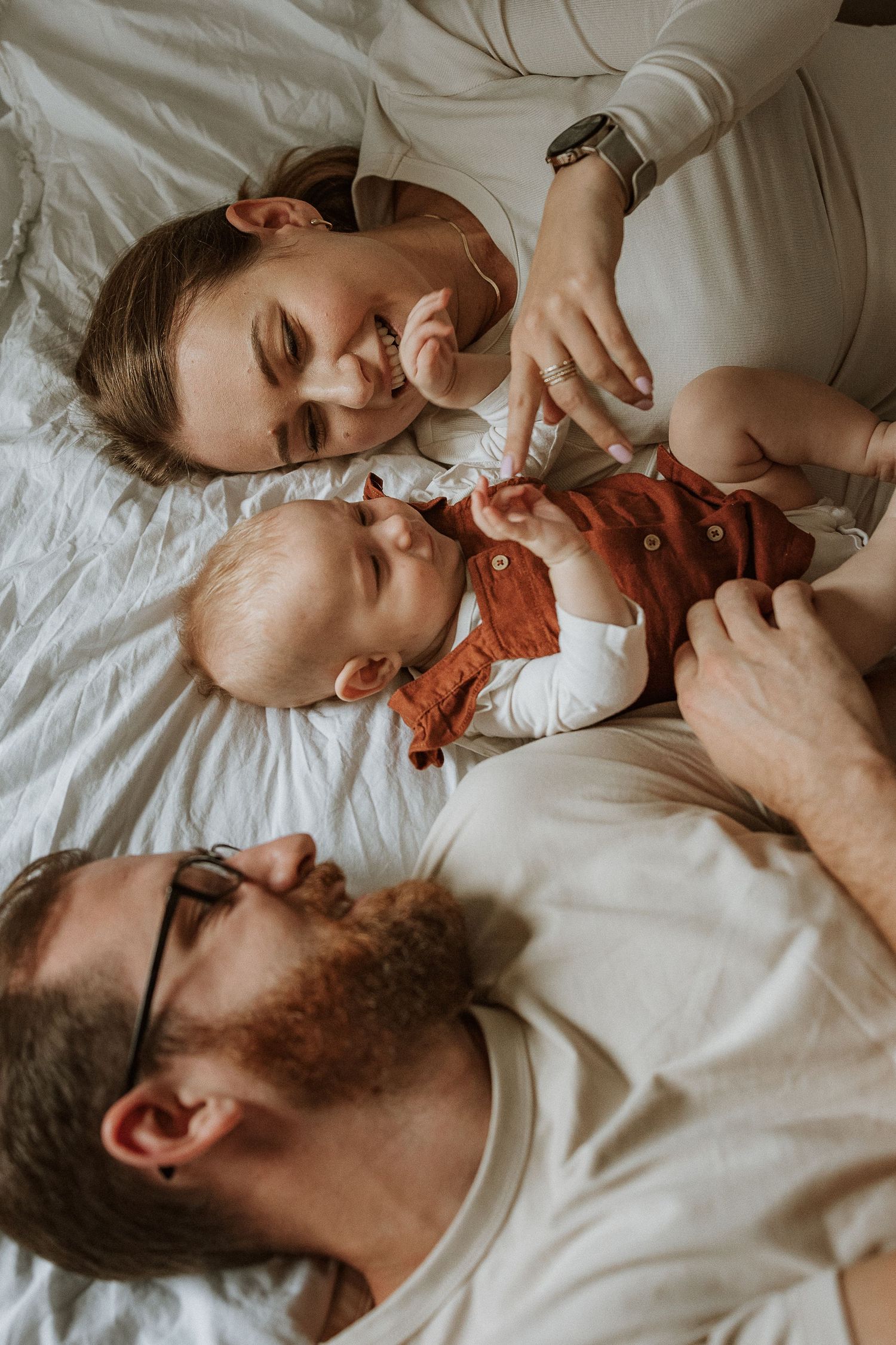 Parent and baby share tender bonding moments while lying together on white bedding.