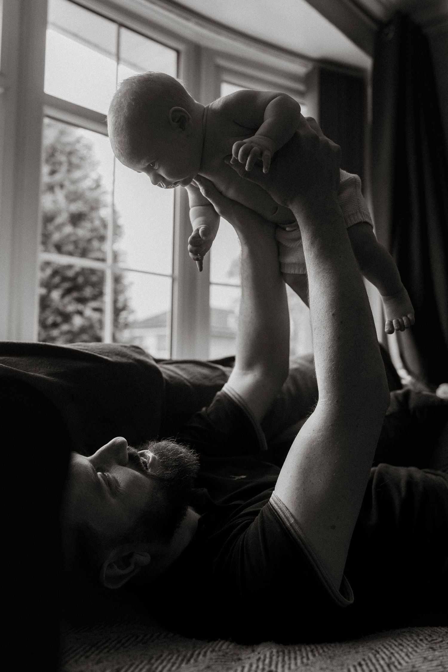 Black and white photo series showing a baby being lifted playfully in the air against a window backdrop.