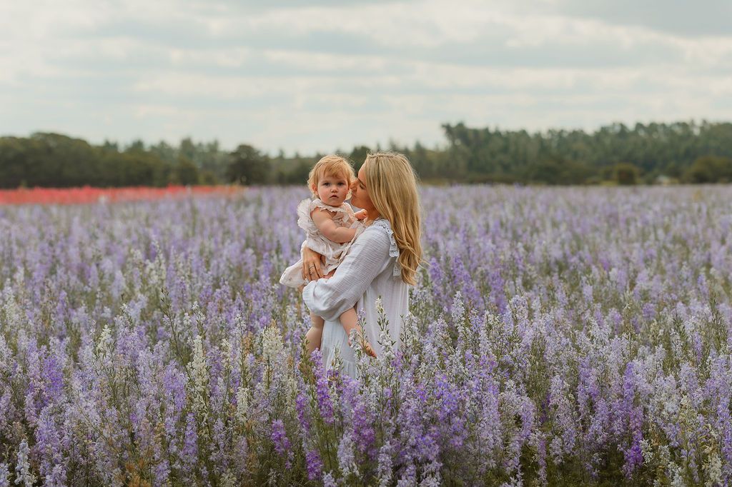 A mother holds her toddler in a blooming lavender field, sharing a tender kiss outdoors.