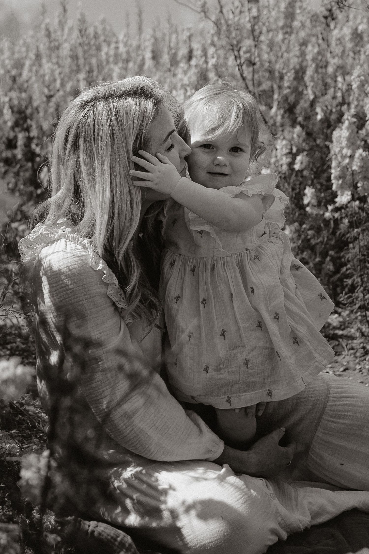A tender black and white portrait of a parent and child sharing an intimate moment among confetti flower fields.