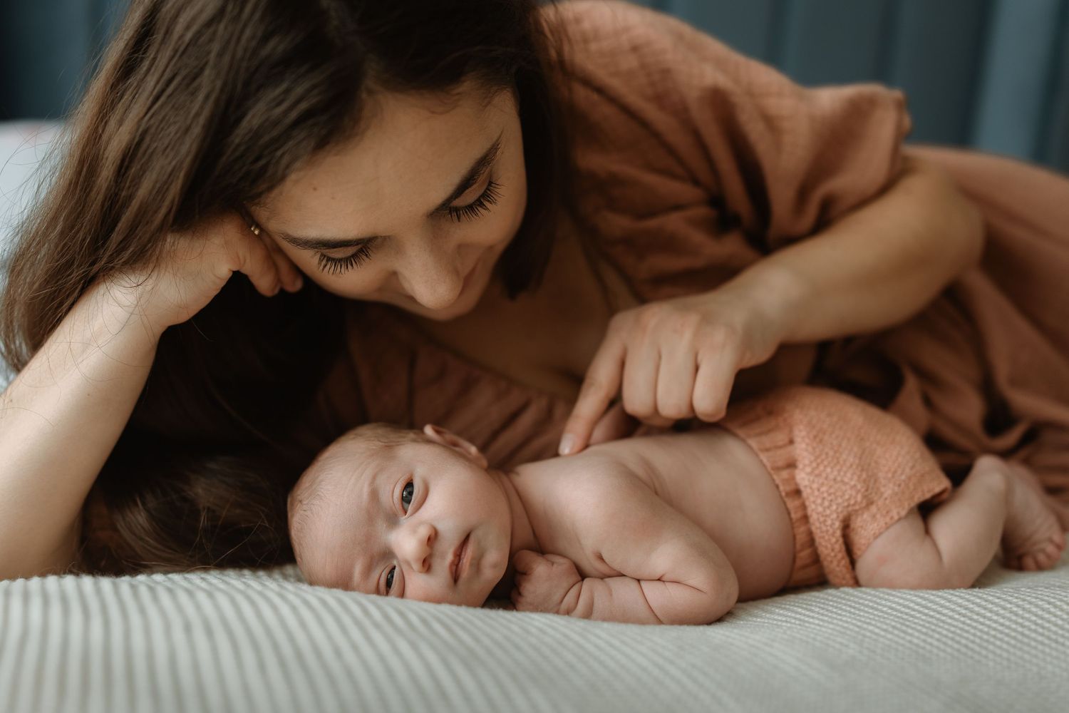 A mother and baby share tender moments together while lying on white bedding in a series of intimate photographs.