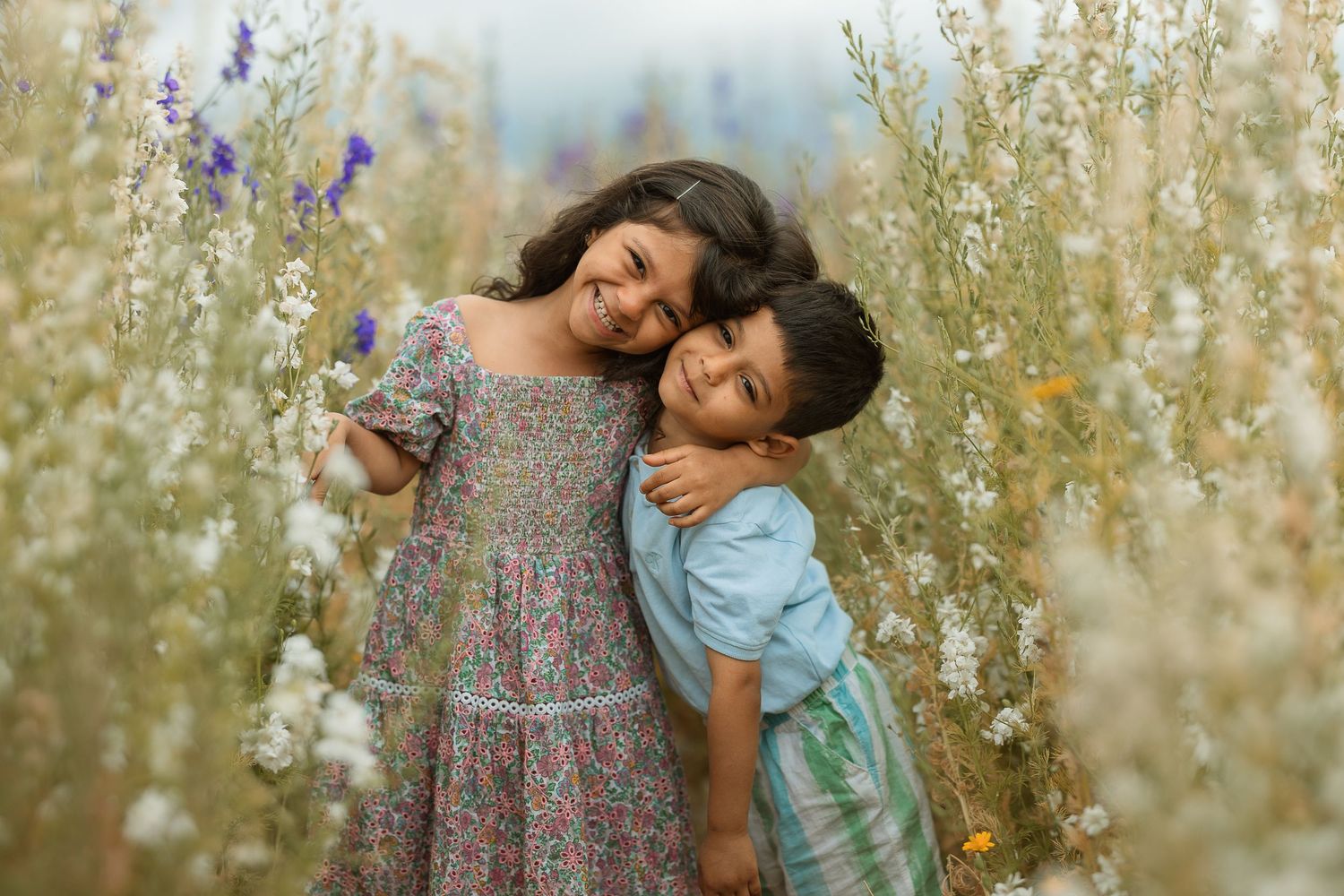 Two people share tender moments in a field of tall wildflowers during a sunny outdoor photo session.