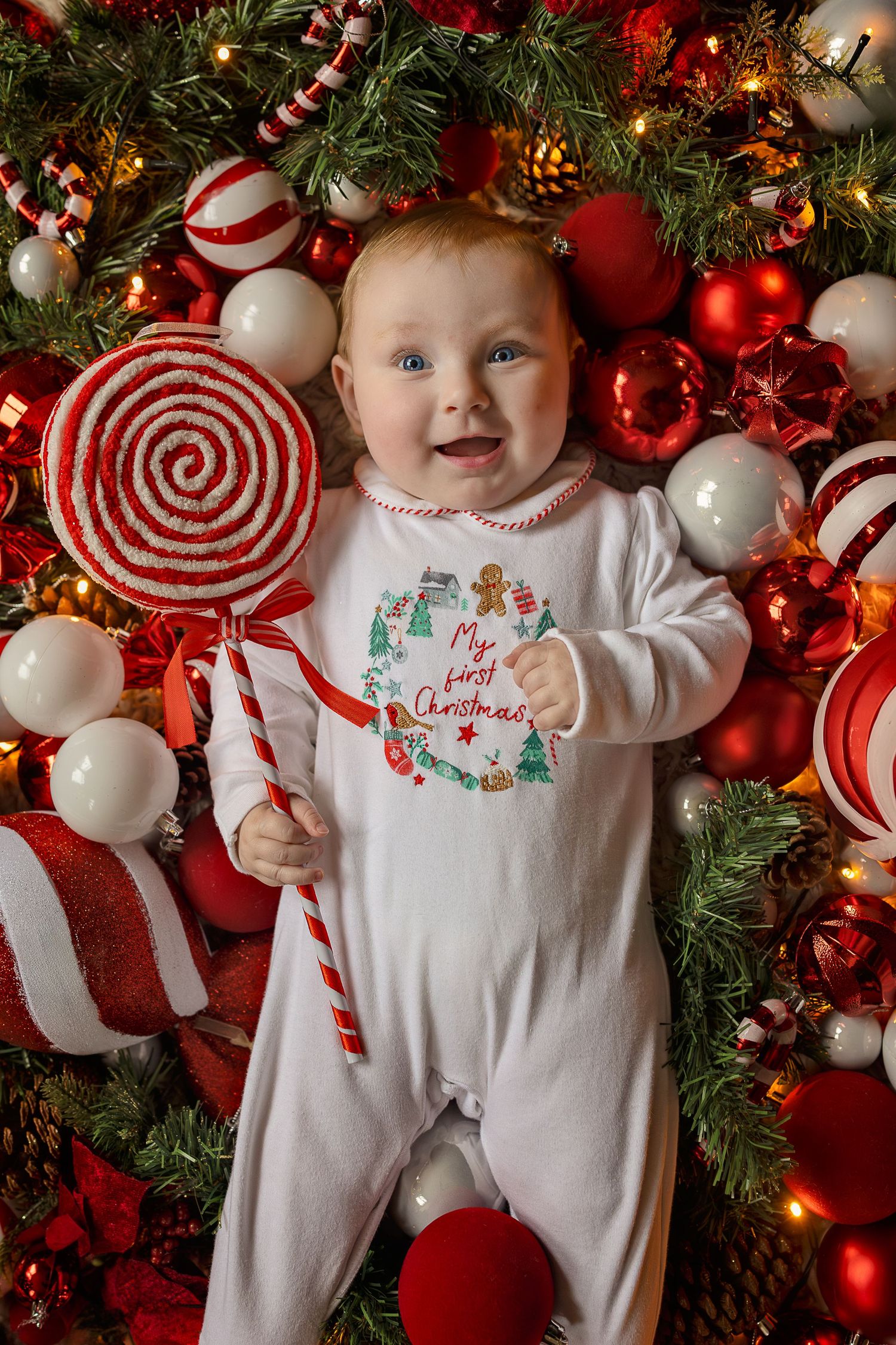 Baby in “My First Christmas” onesie surrounded by red and white ornaments and candy cane decorations.