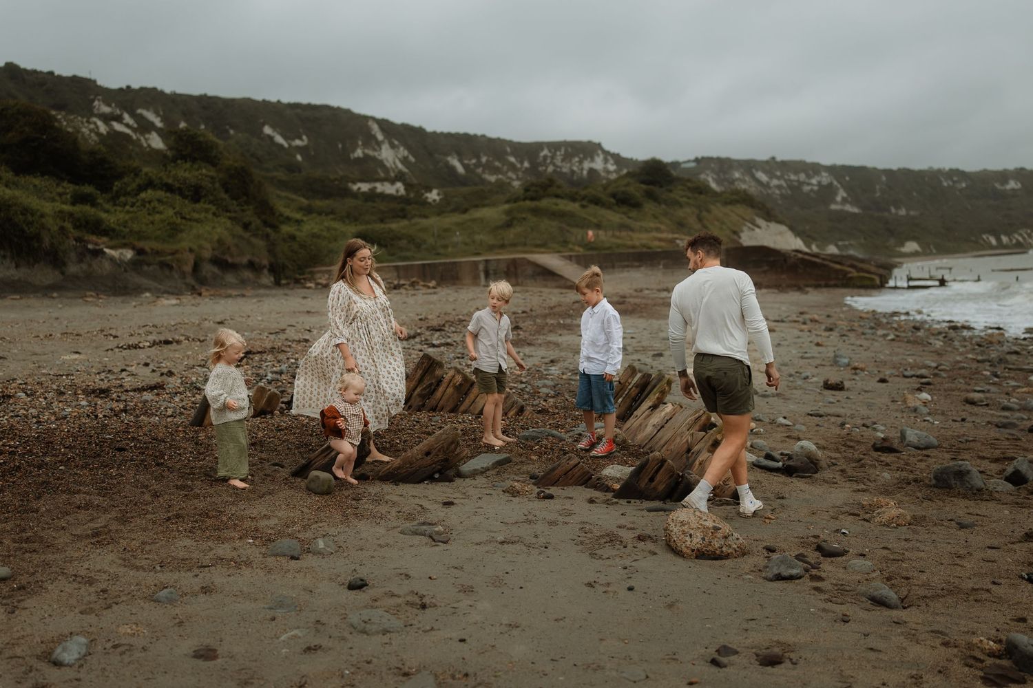 Family enjoying a scenic coastal walk along a rocky beach with dramatic cliffs in the background.
