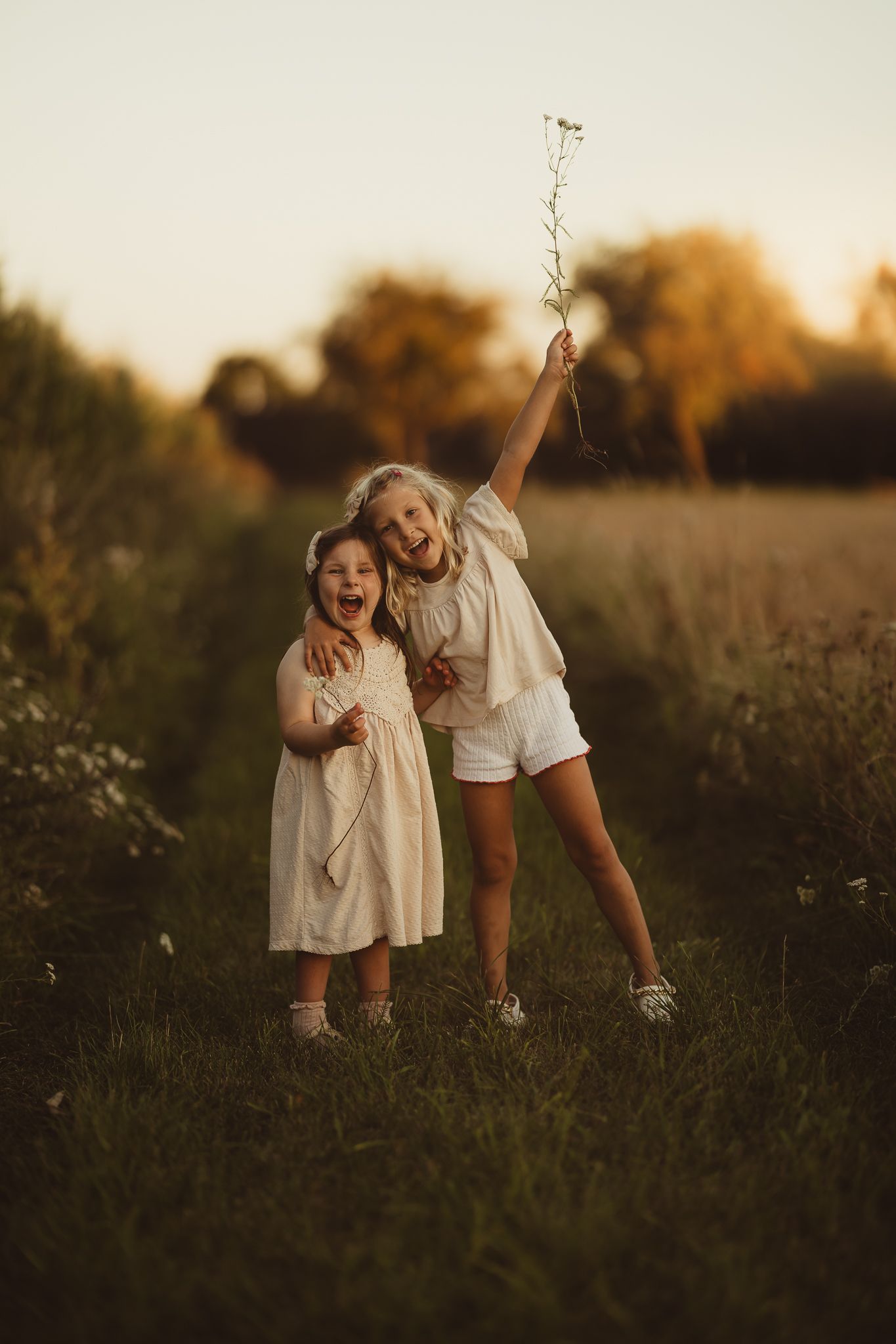 Two people share joyful moments together in a golden-lit meadow at sunset.