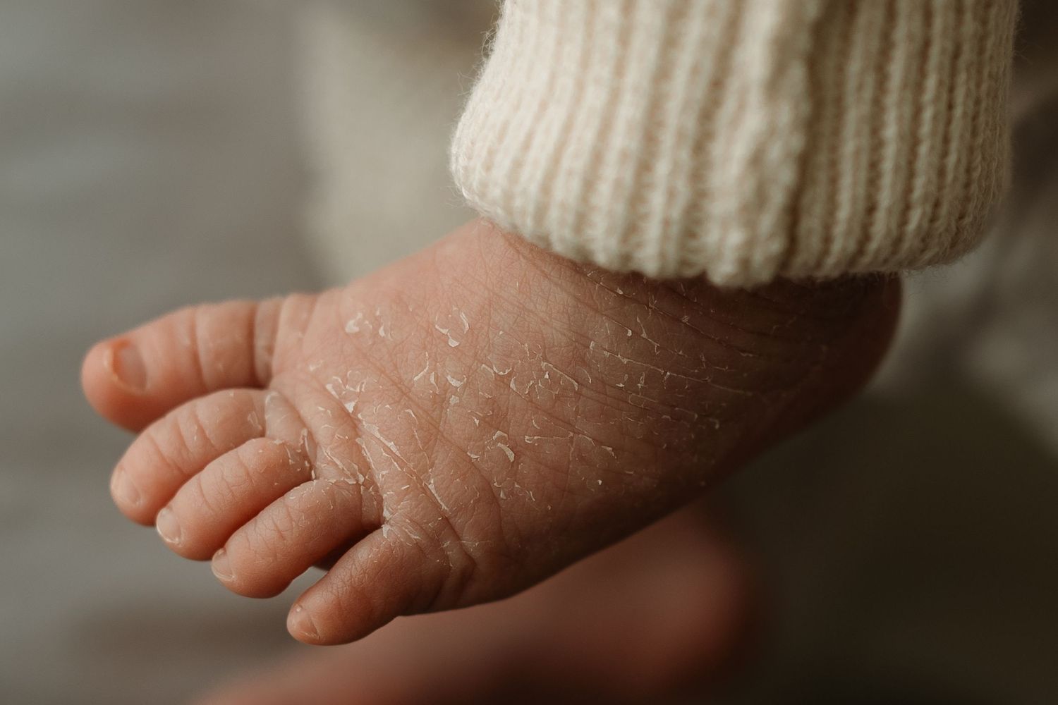 A tiny baby's foot wearing a white knitted bootie against a soft blurred background.
