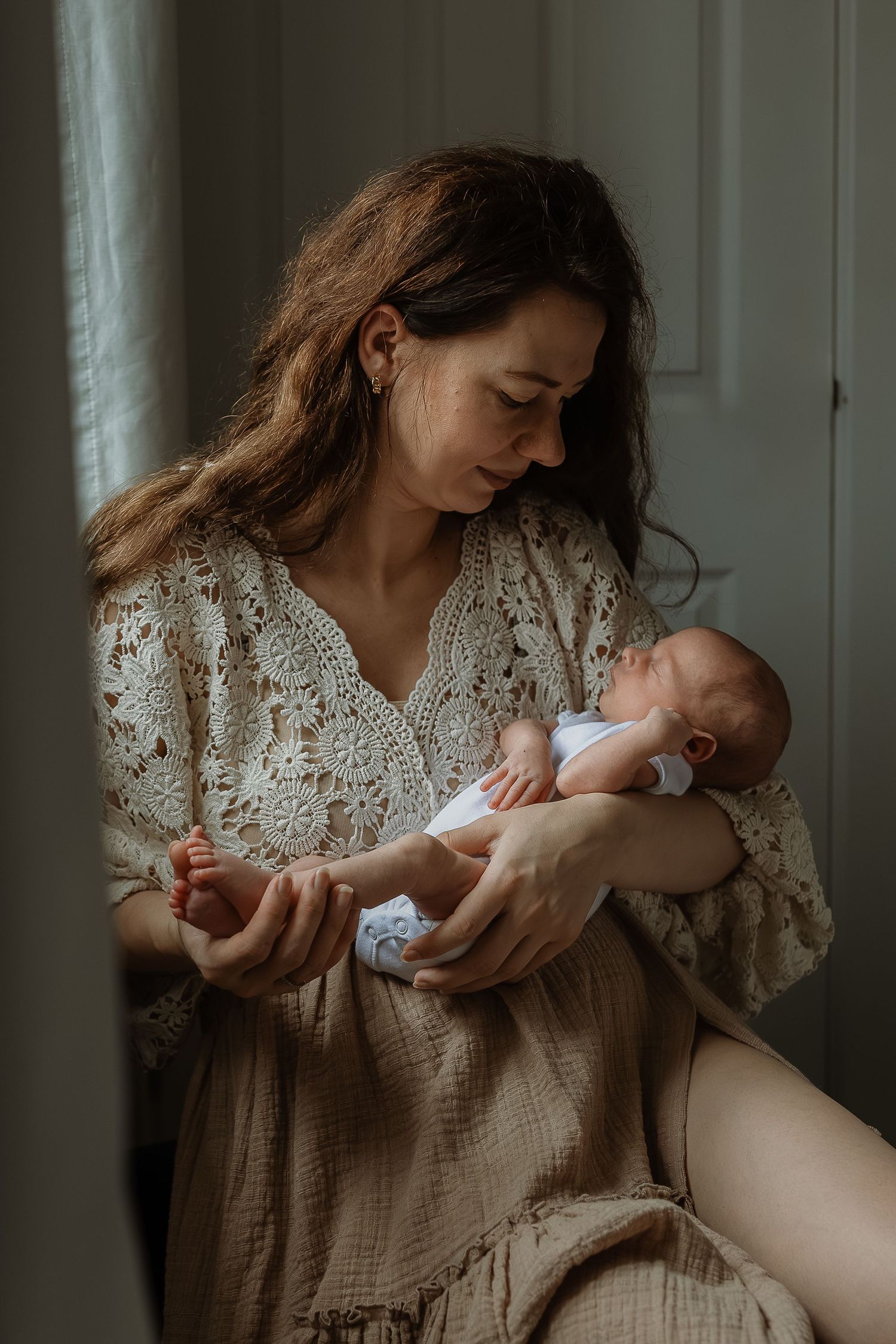 A series of intimate photos showing a mother in a white lace dress holding and bonding with her newborn baby.