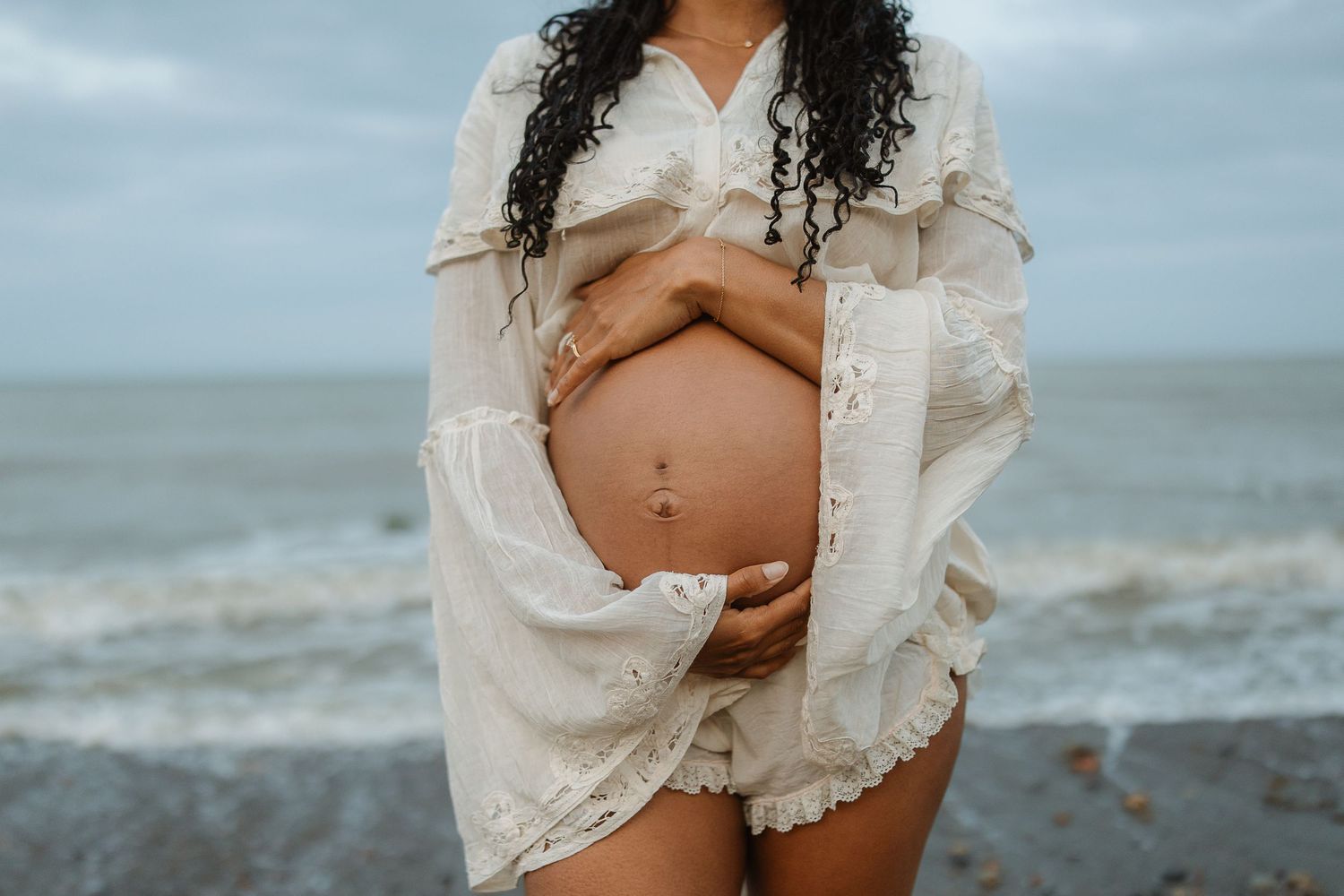 A series of beachside maternity photos showing a flowing white lace dress against a misty ocean backdrop.