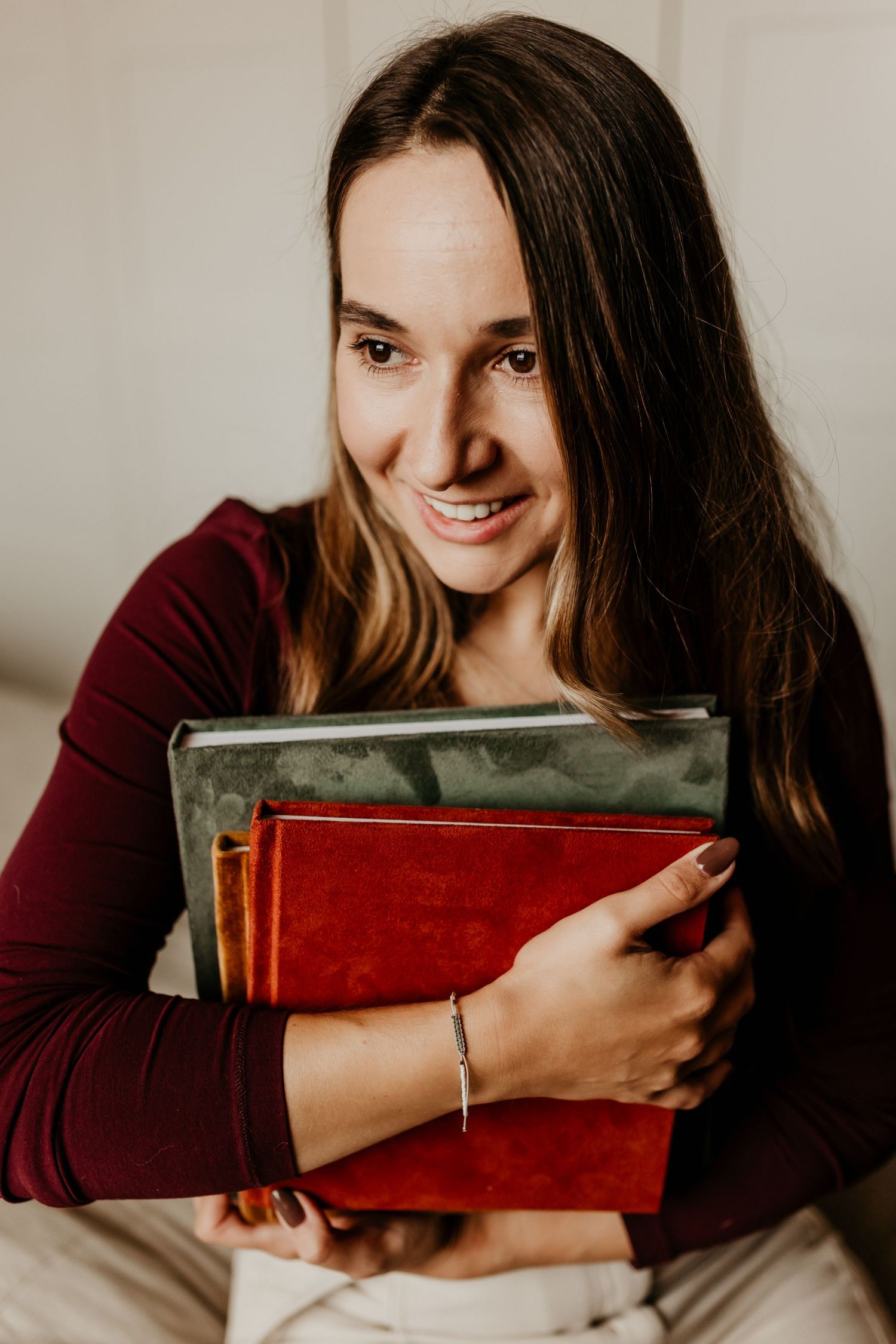 A series of photos showing someone in a burgundy sweater hugging and smiling with a vintage red book against a neutral background.